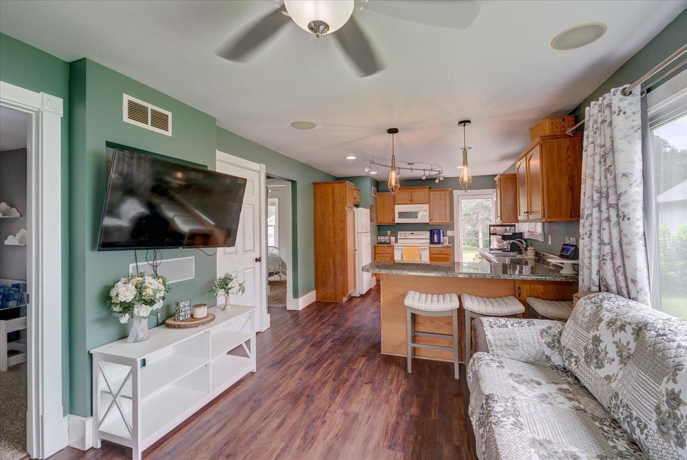Open-plan kitchen and living area with a granite island, green walls, wood cabinetry, and patterned sofa.