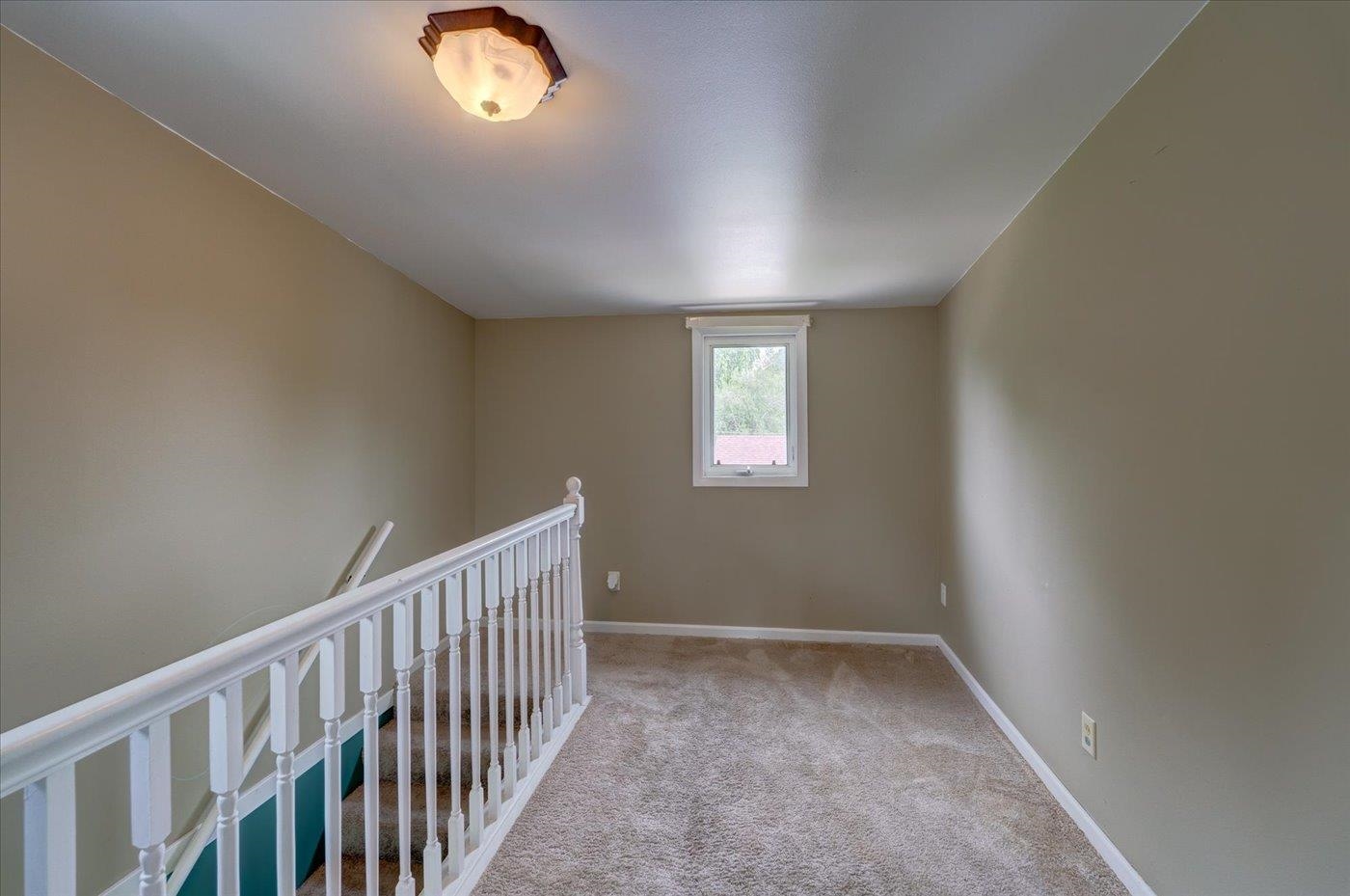 Carpeted upstairs landing with a white stair railing and small window.