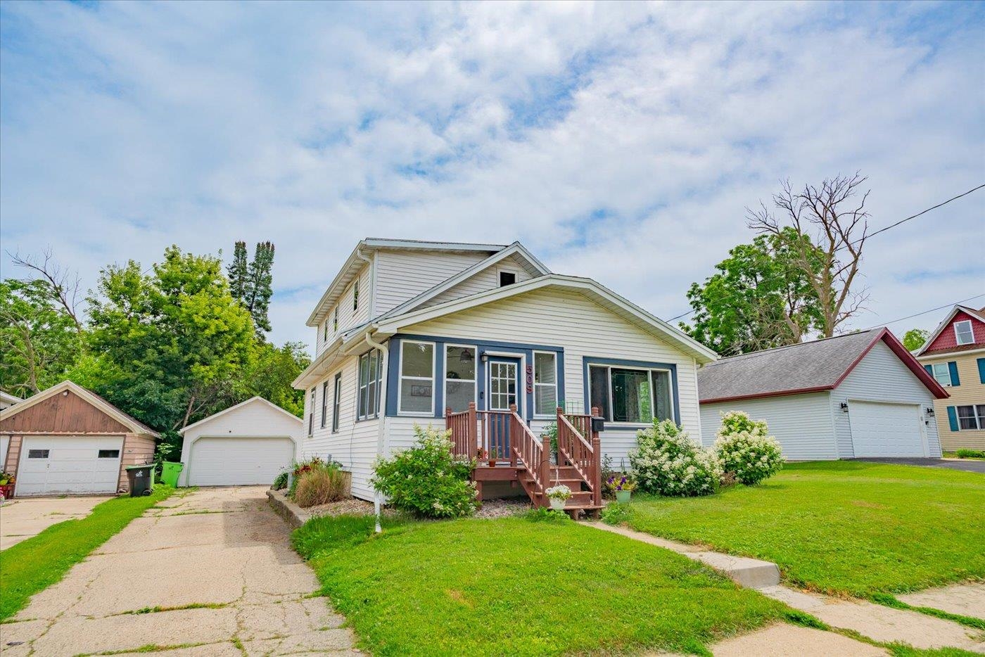 White two-story house with blue trim, a wooden front porch, and detached garages nearby.