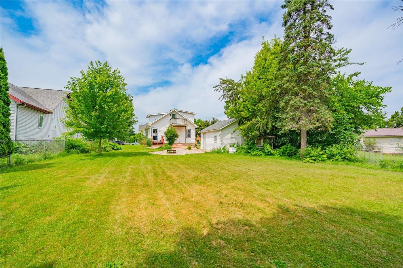Backyard with a broad lawn, mature trees, and the house beyond.