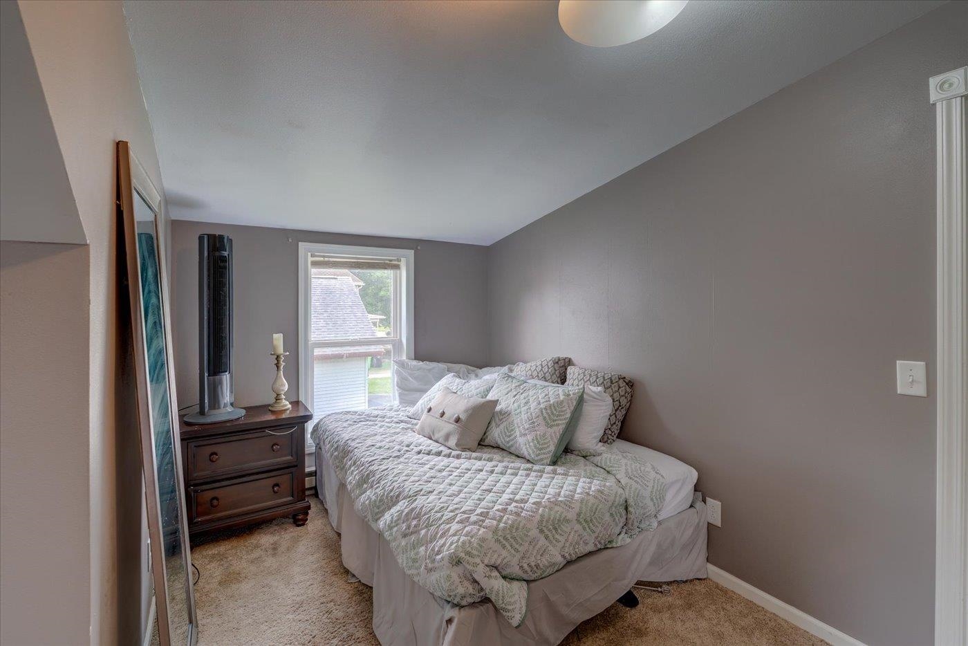 Bedroom with a patterned quilt, gray walls, and a window beside the bed.