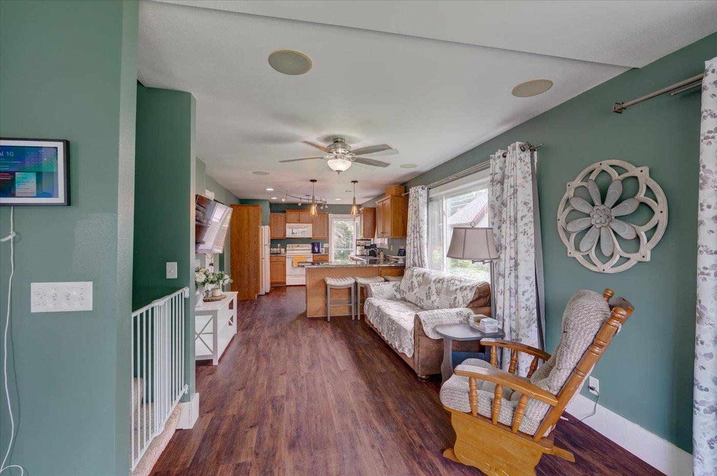 Open living room and kitchen with teal walls, patterned sofa, and dark wood-look flooring.