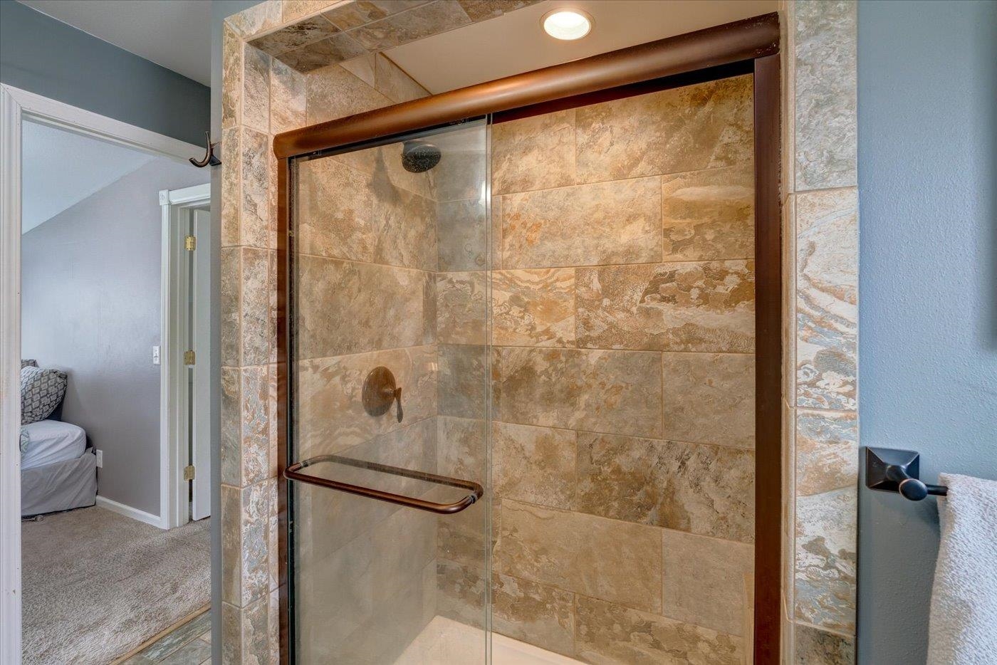 Walk-in shower with patterned stone tile, glass enclosure, and bronze-colored fixtures.