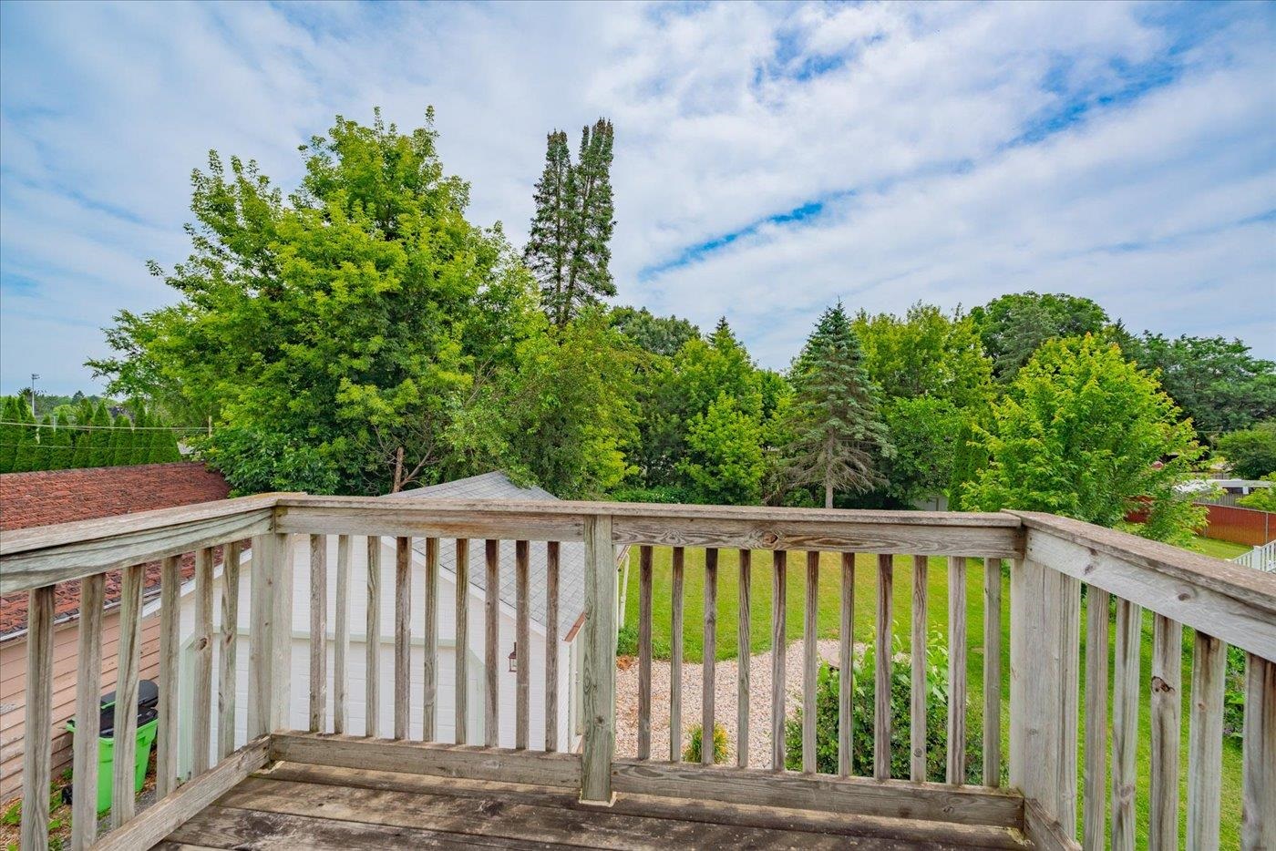 Wooden deck overlooking a leafy backyard with mature trees and lawn.