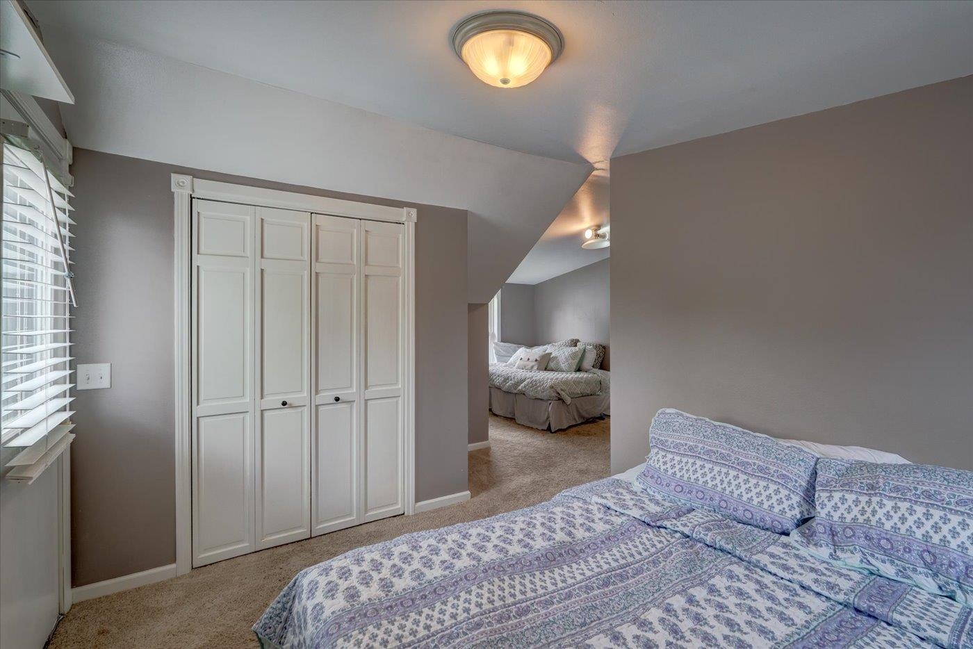 Bedroom with two beds, patterned bedding, a white closet, and a sloped ceiling.