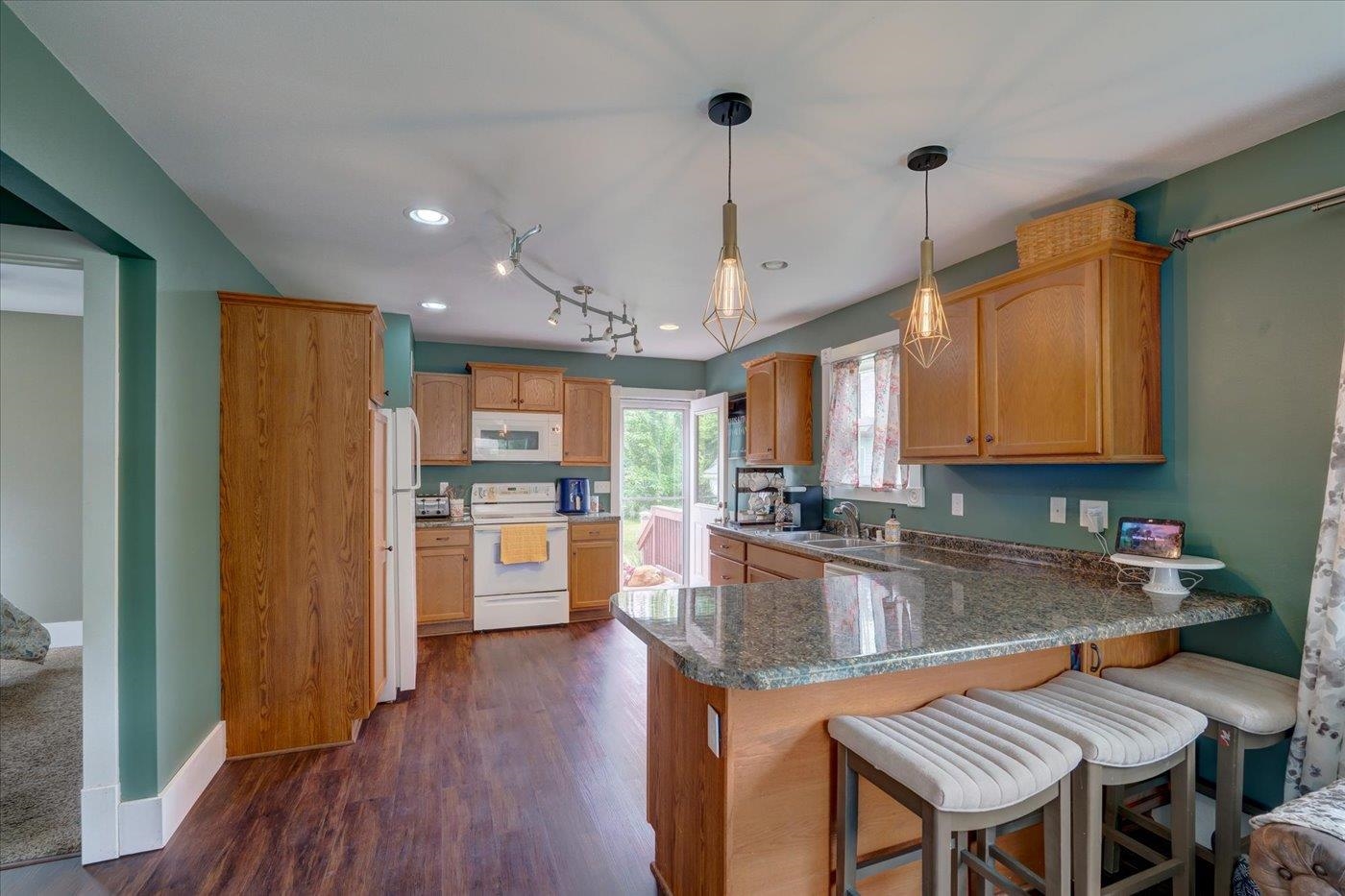 Kitchen with teal walls, wood cabinets, granite island, and upholstered bar stools.