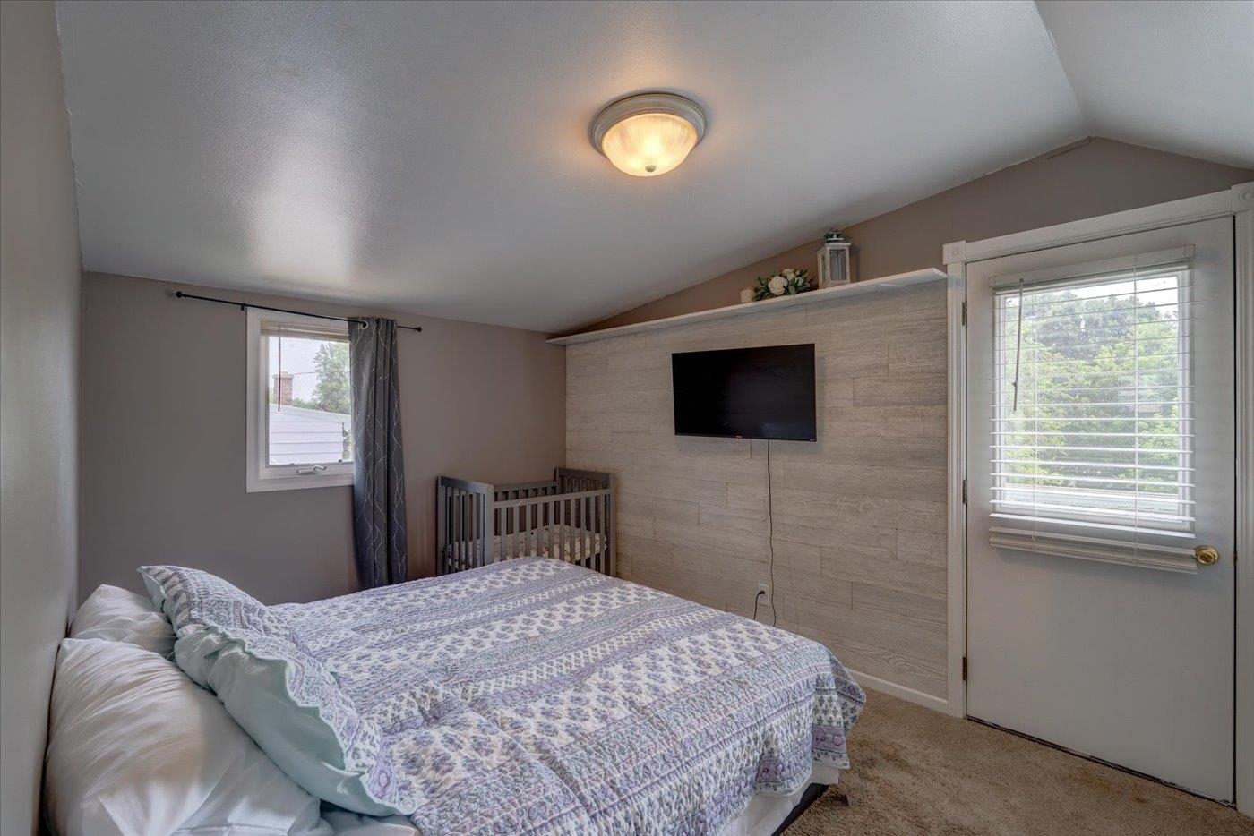Furnished bedroom with a wooden crib and television mounted on a light accent wall.