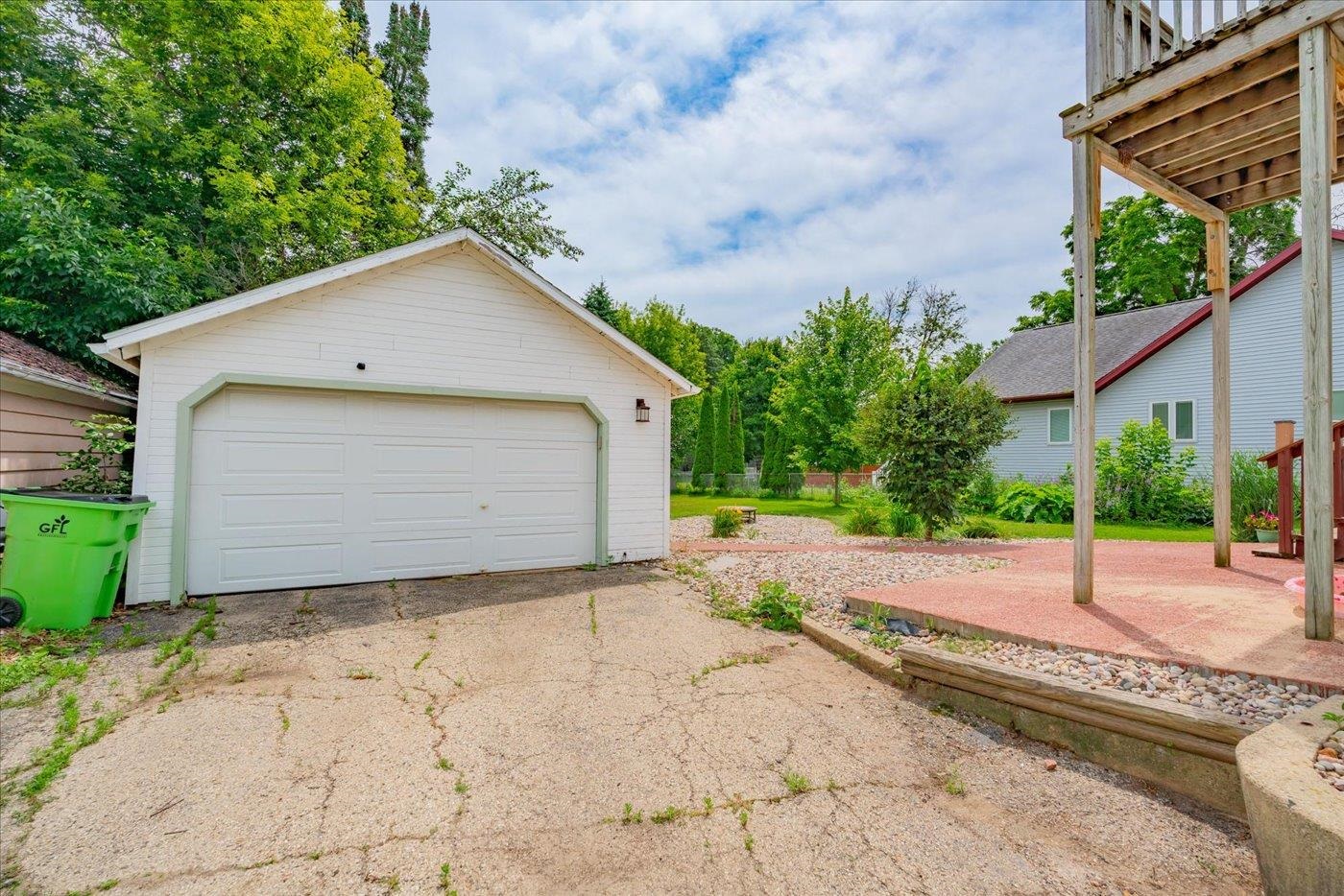 White detached garage beside a cracked driveway, landscaped yard, and raised wooden deck.