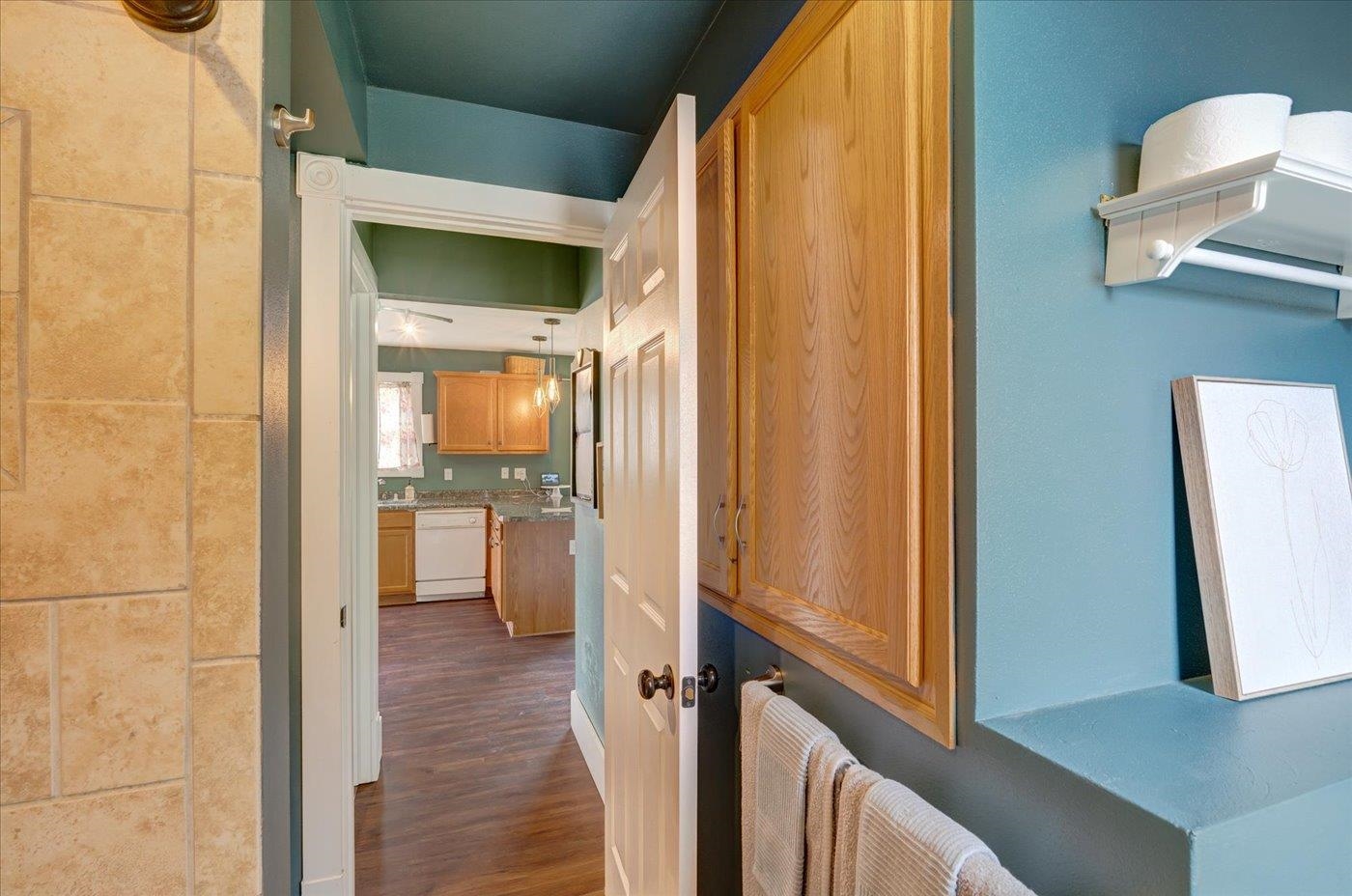 Bathroom with tan tile, teal walls, a wooden cabinet, and an open doorway to the kitchen.