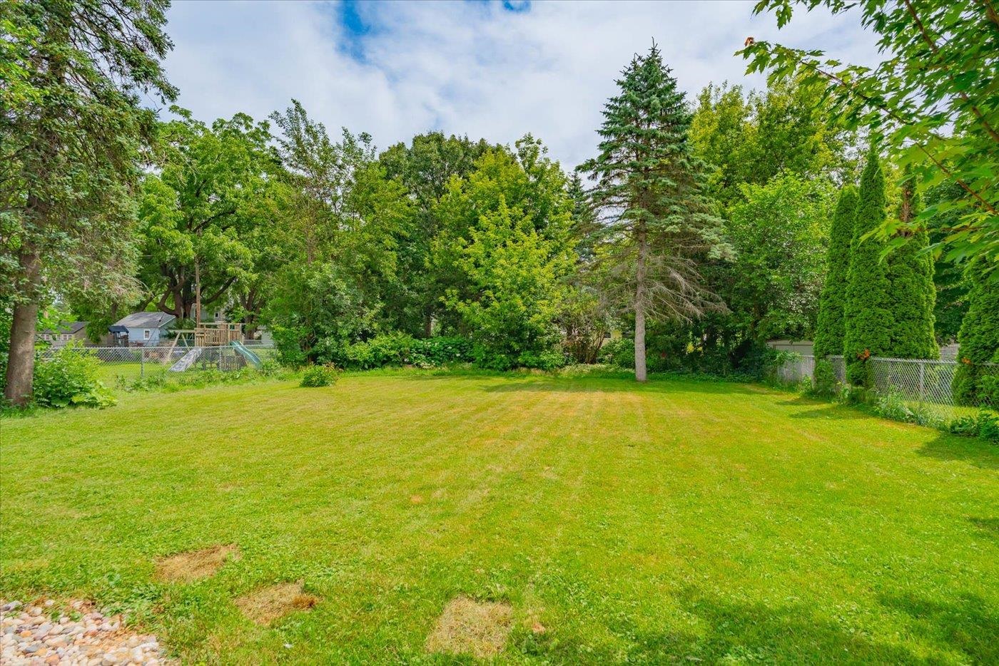 Spacious backyard lawn bordered by mature trees and fencing.