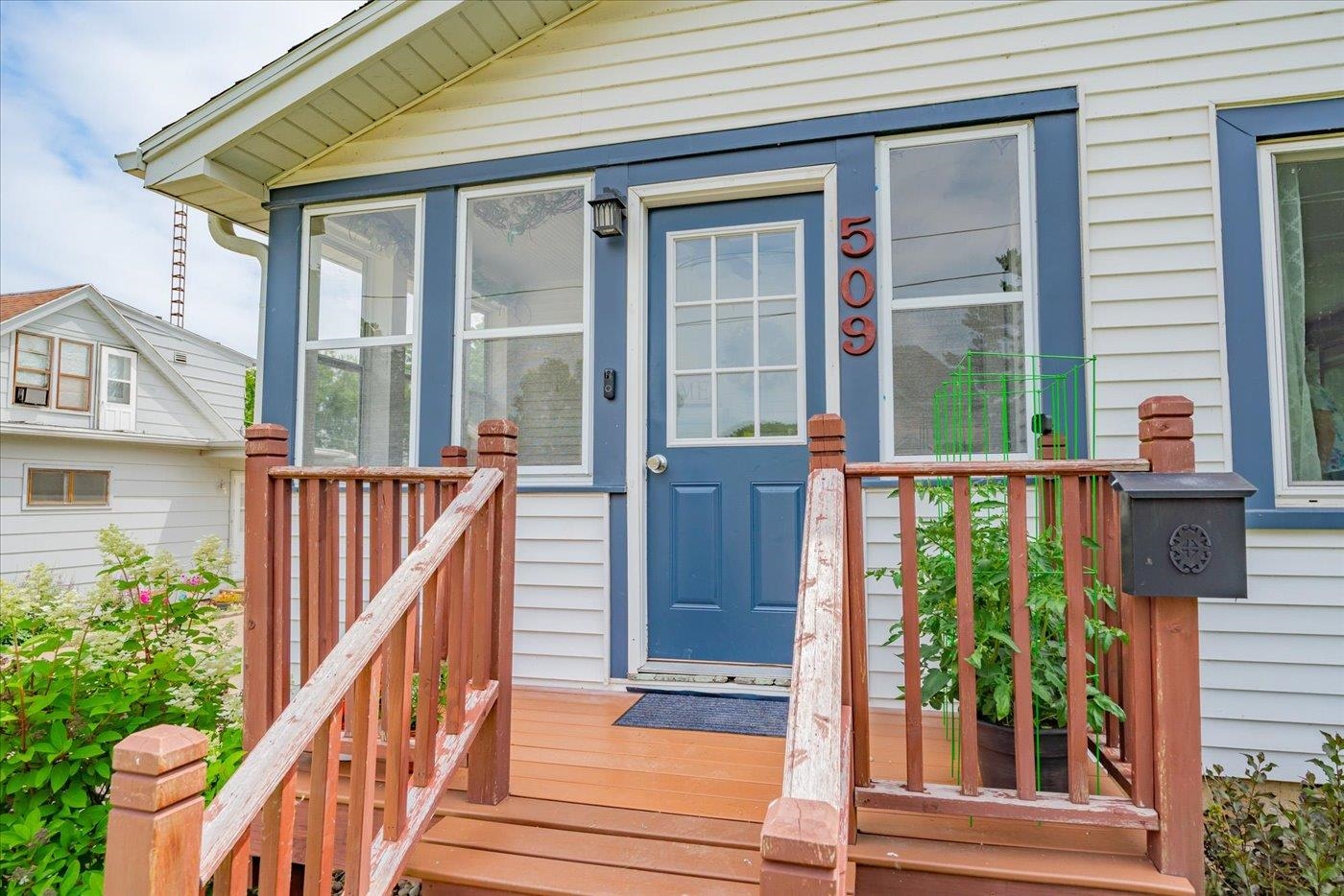 House entrance with blue door numbered 509, raised wooden porch, and reddish-brown steps and railings.