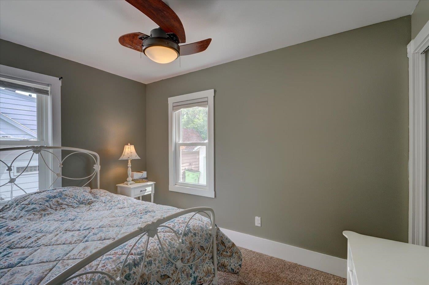 Bedroom with a floral-quilted metal bed, olive-gray walls, two windows, and a ceiling fan.