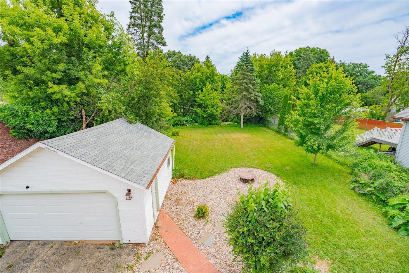 Backyard with a broad lawn, mature trees, detached garage, gravel fire-pit area, and raised deck.