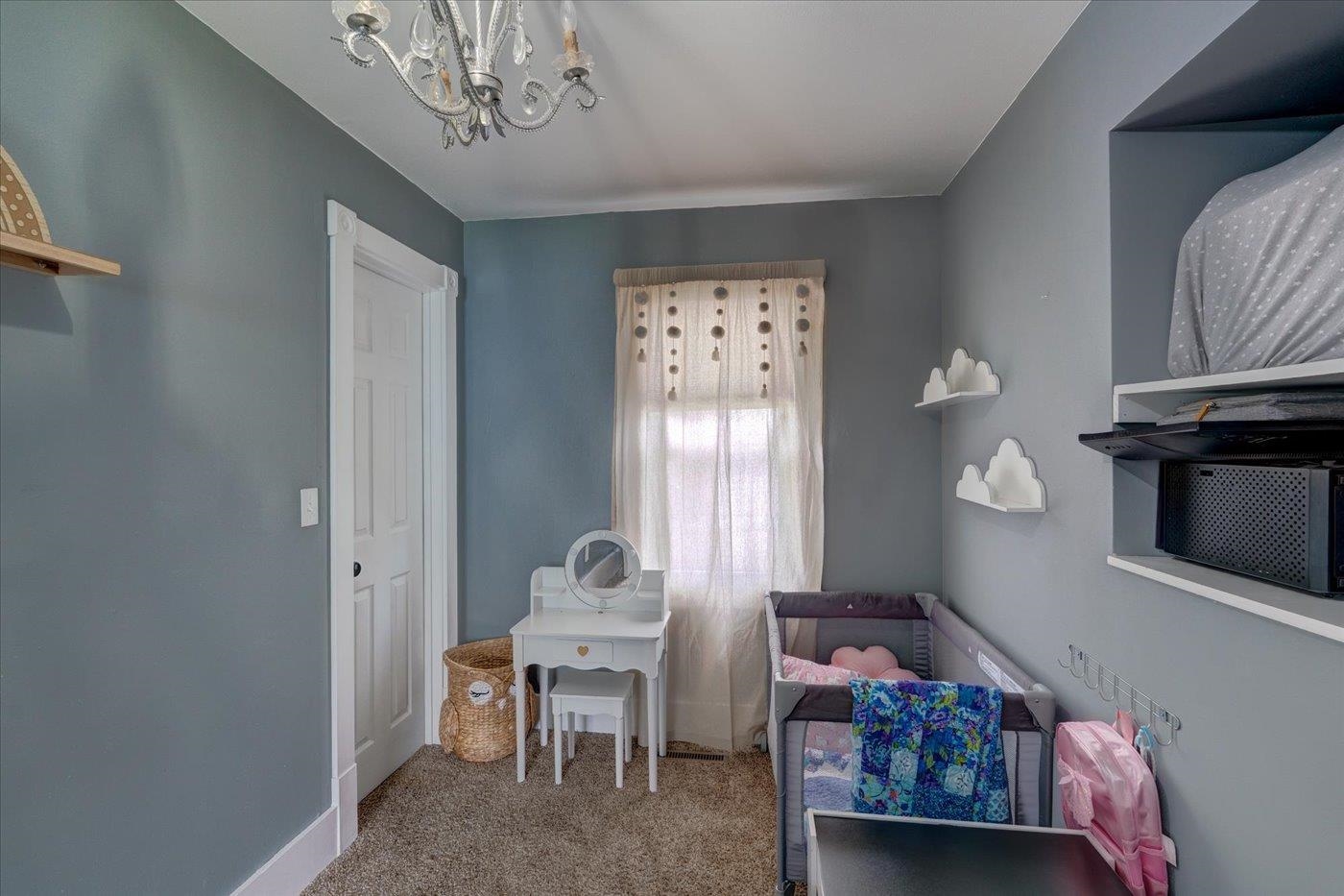 Nursery with a crib, white vanity, curtained window, and chandelier.