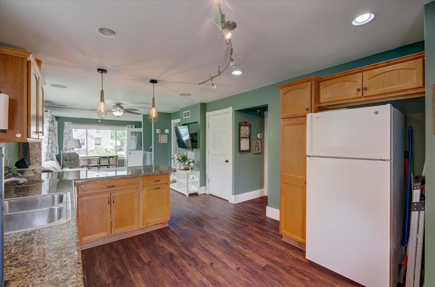 Kitchen with wood cabinets, granite counters, a large white refrigerator, and adjoining sitting area.