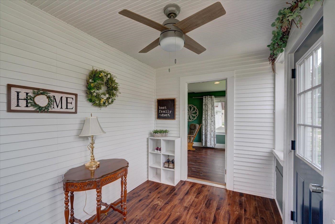 Enclosed porch with white shiplap walls, wood-look flooring, and tall windows beside the entry door.