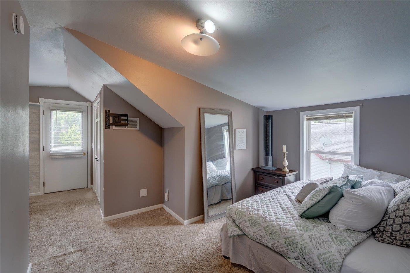Attic bedroom with a sloped ceiling, patterned bedding, beige carpet, and a full-length mirror.