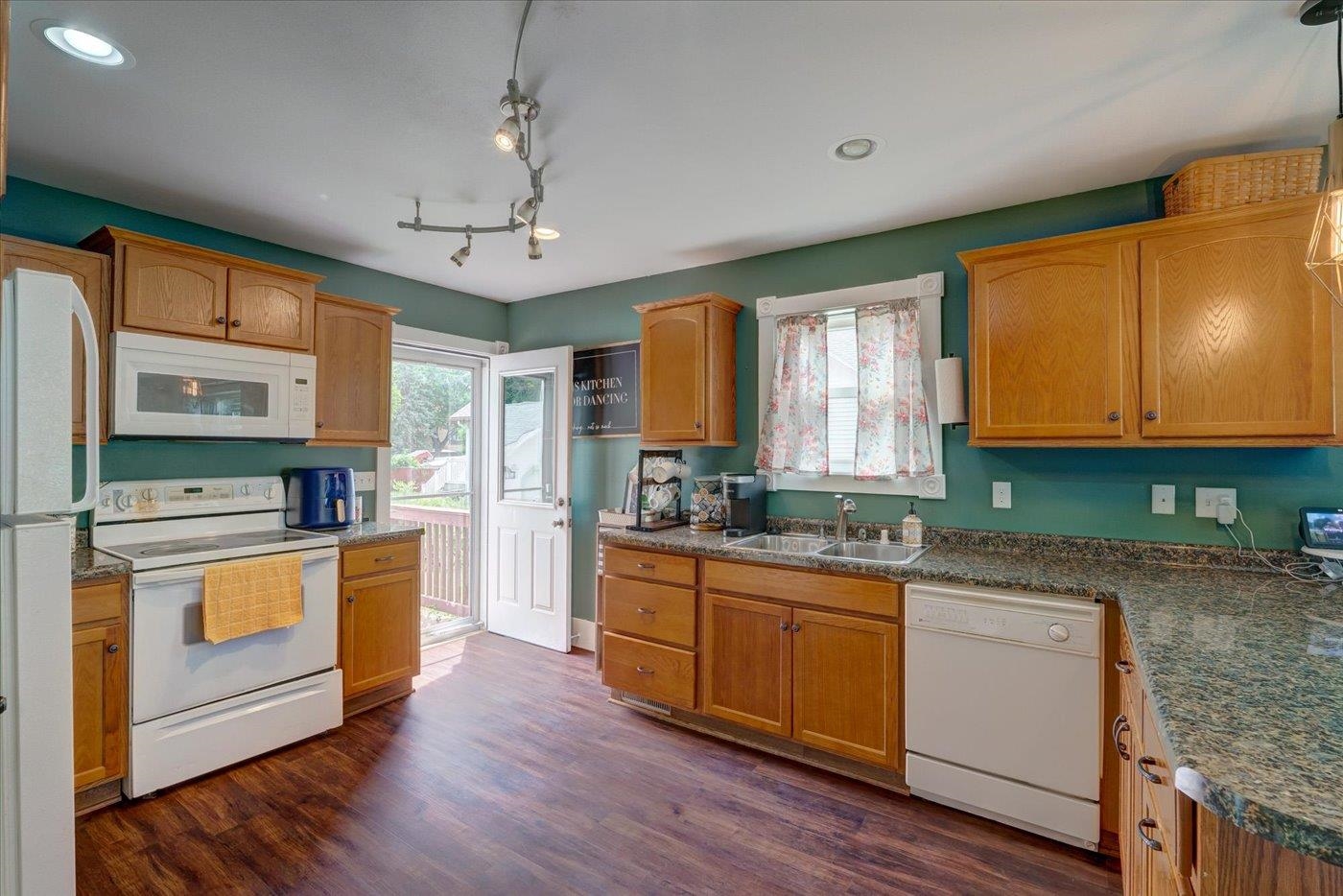 Kitchen with teal walls, wood cabinets, granite counters, and an open door to a deck.