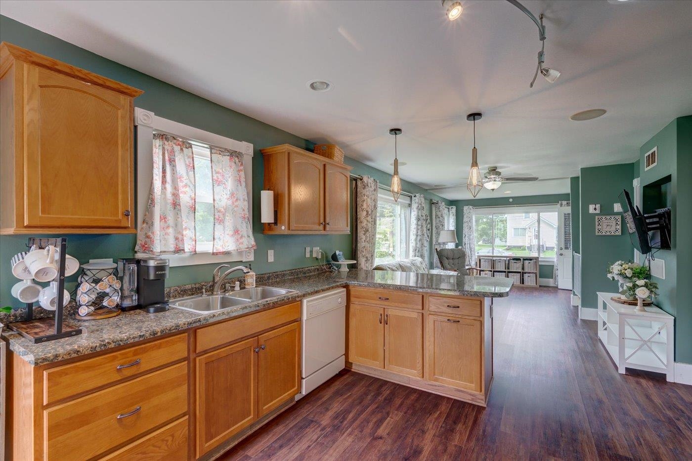 Kitchen with wood cabinets and granite counters, opening into a bright living area with large windows.