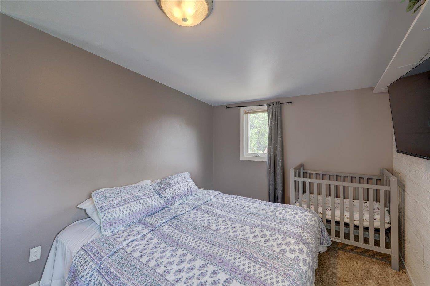 Bedroom with a patterned bedspread and a crib beside the window.
