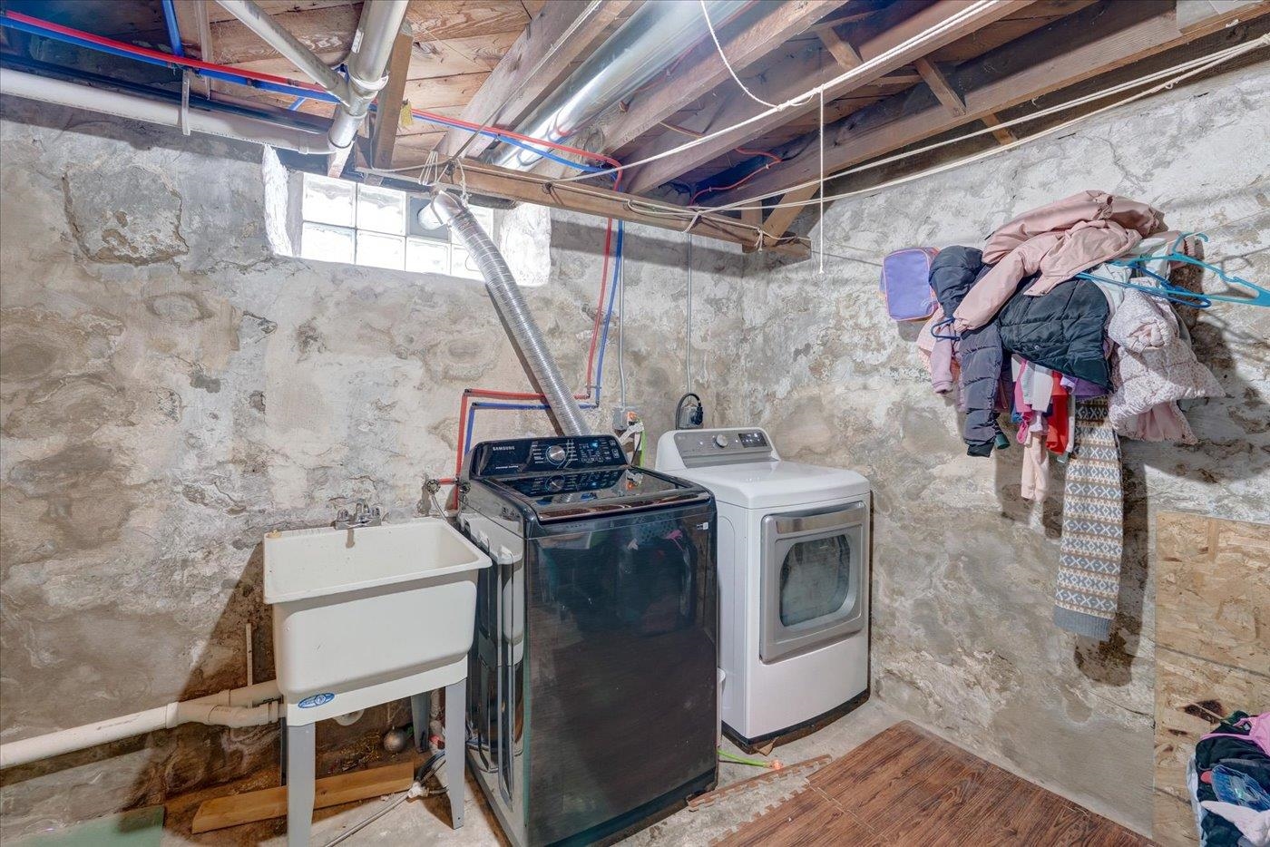 Basement laundry room with washer, dryer, utility sink, and exposed stone walls.