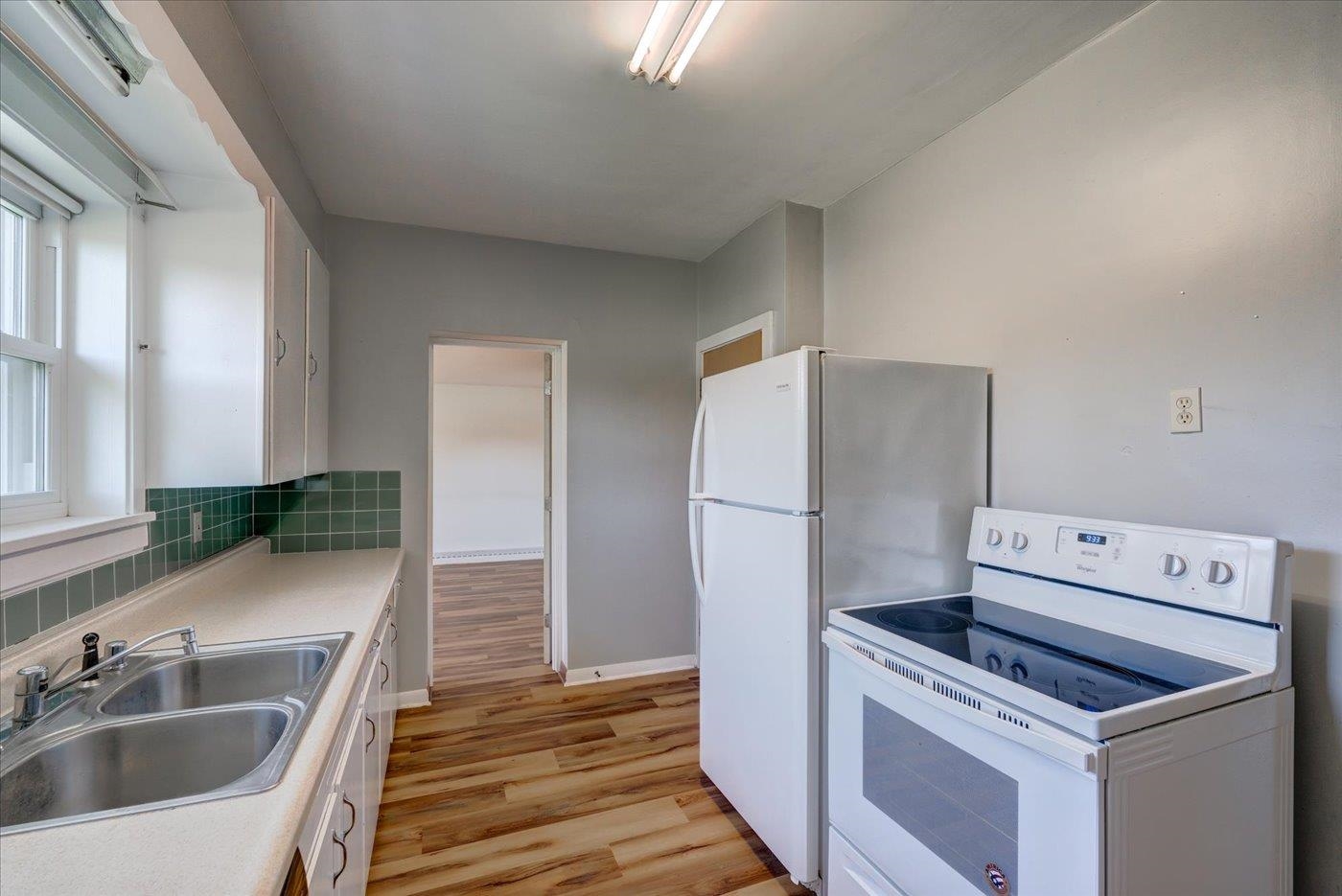 Kitchen with green tile backsplash, double-basin sink, white appliances, and wood-look flooring.