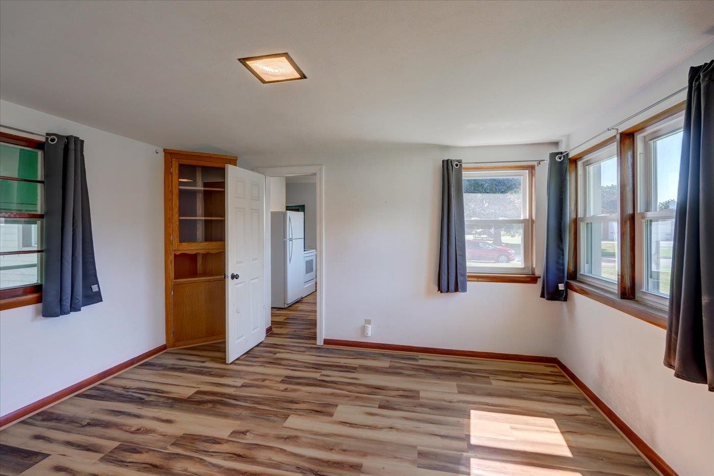 Empty room with wood-look flooring, curtained windows, and built-in shelving.