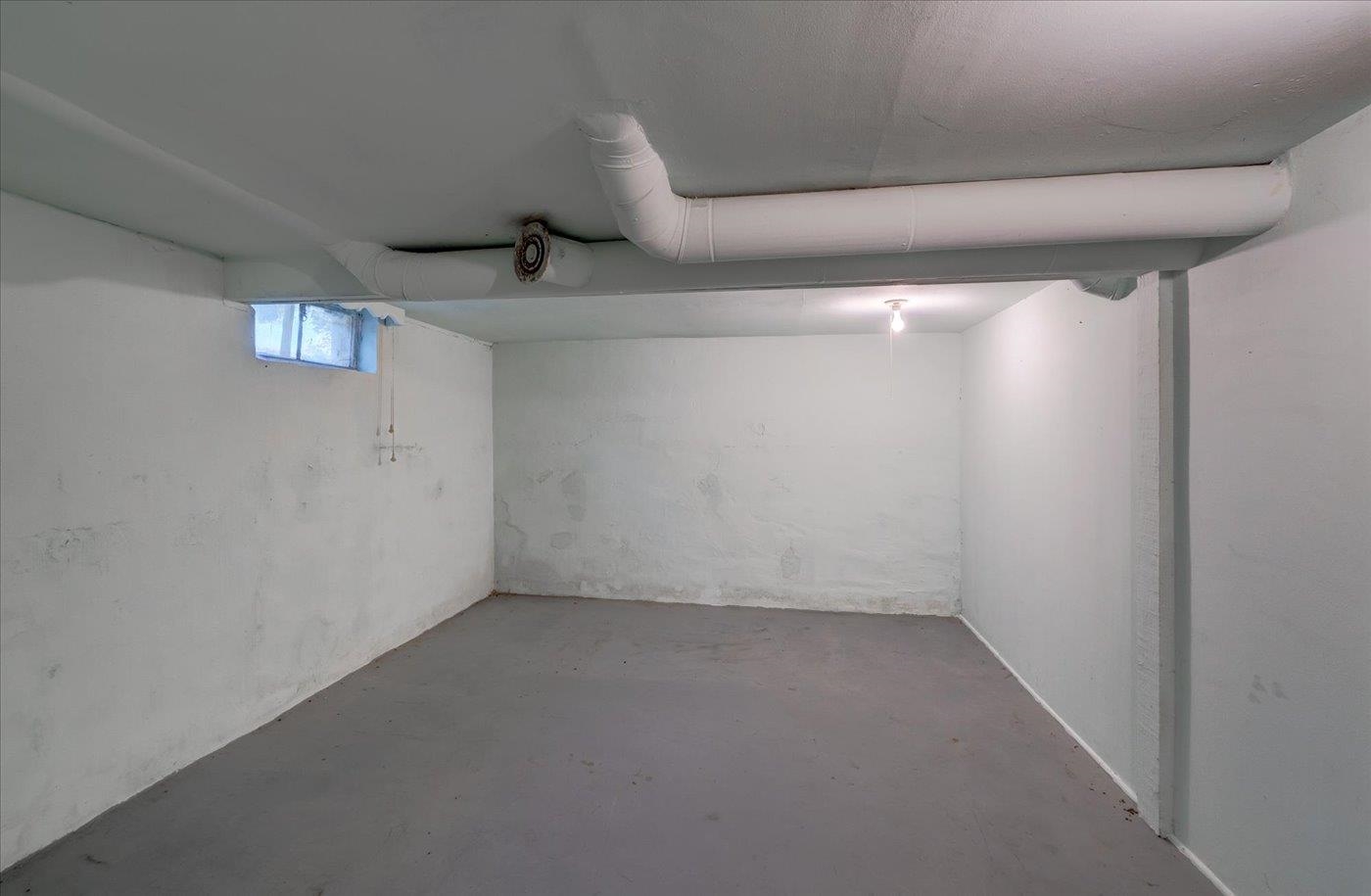 Empty basement with exposed overhead ductwork and a small high window.