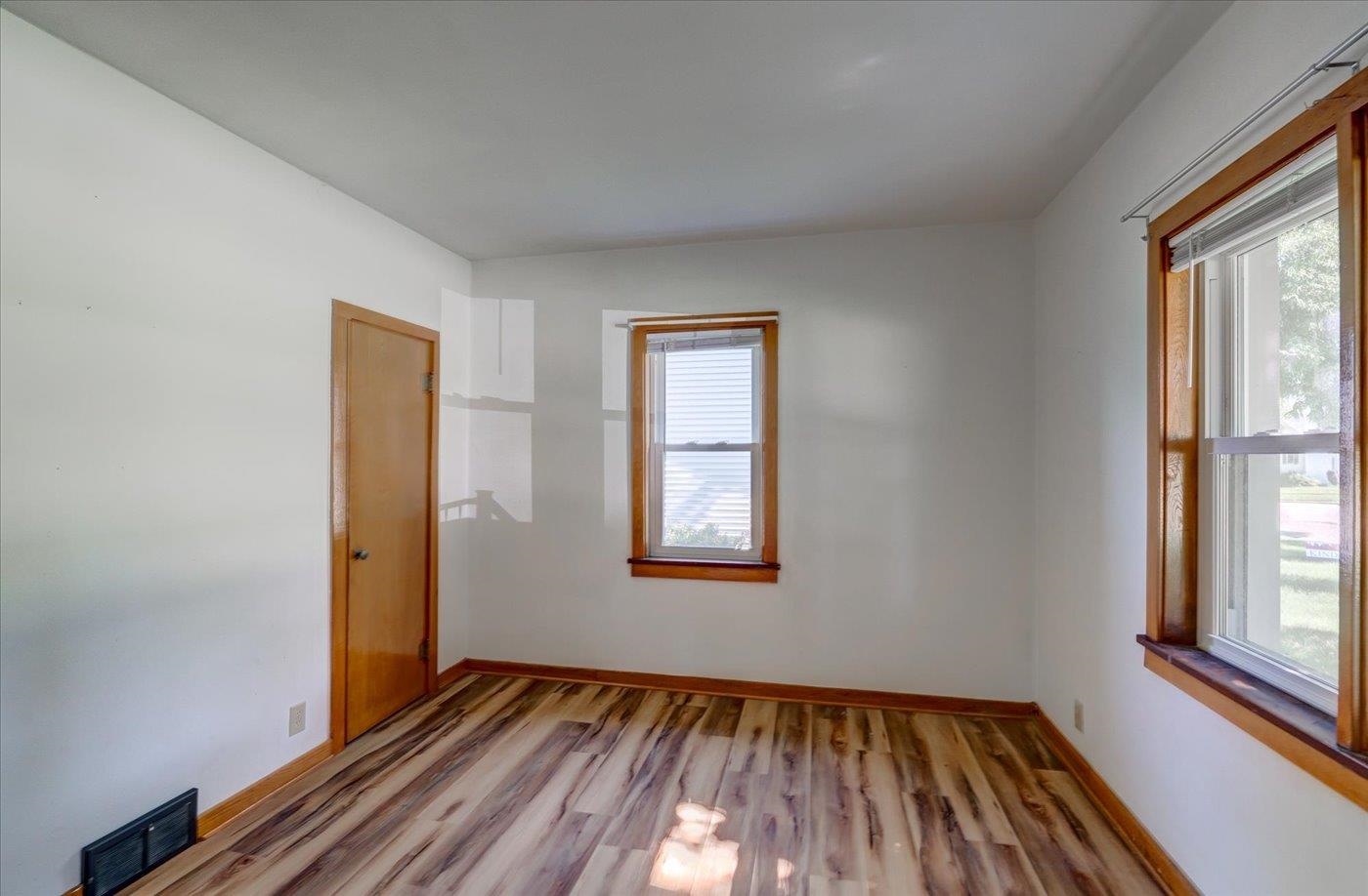 Empty room with wood-look flooring, wood-trimmed windows, and a door.