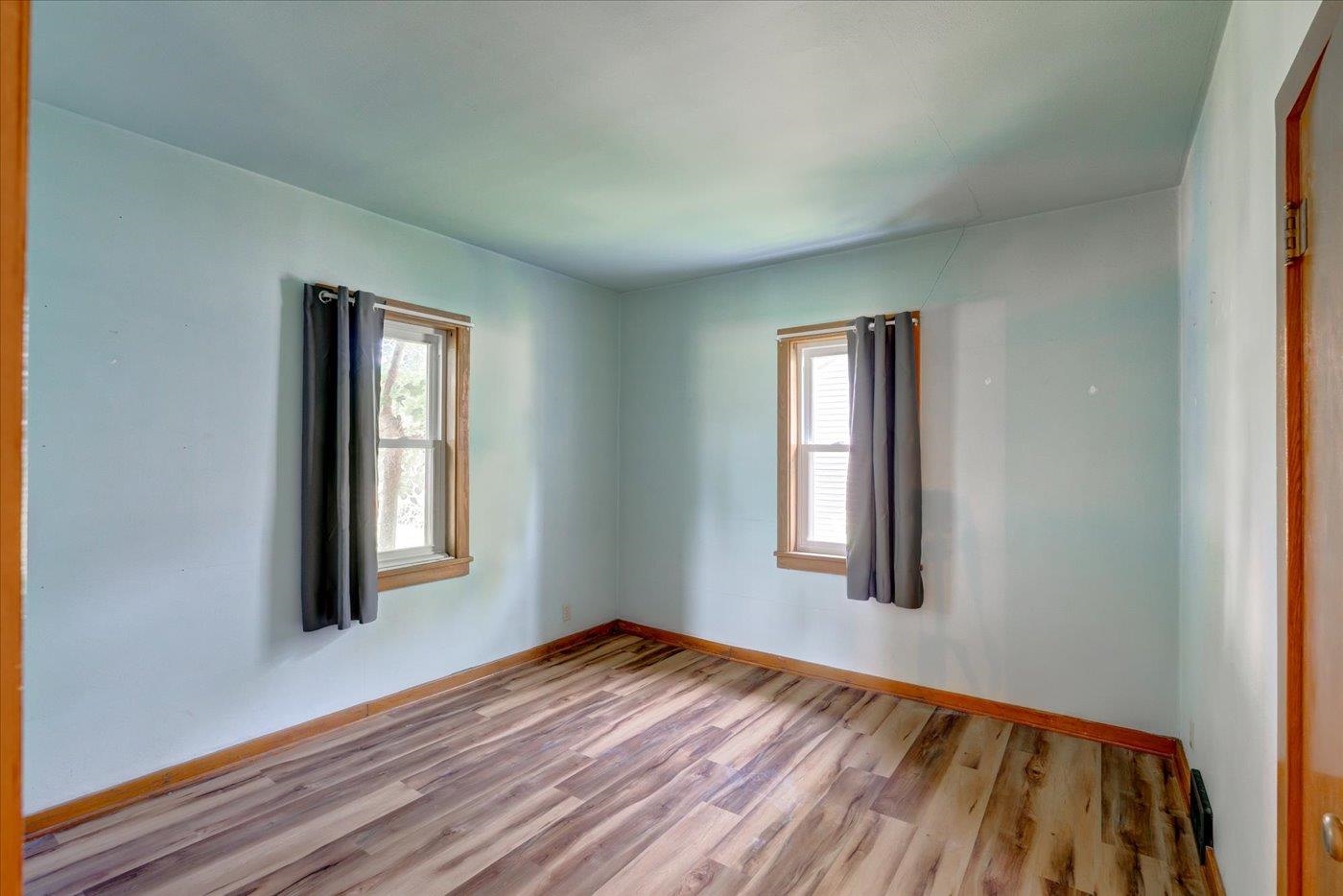 Empty room with two curtained windows and wood-look flooring.