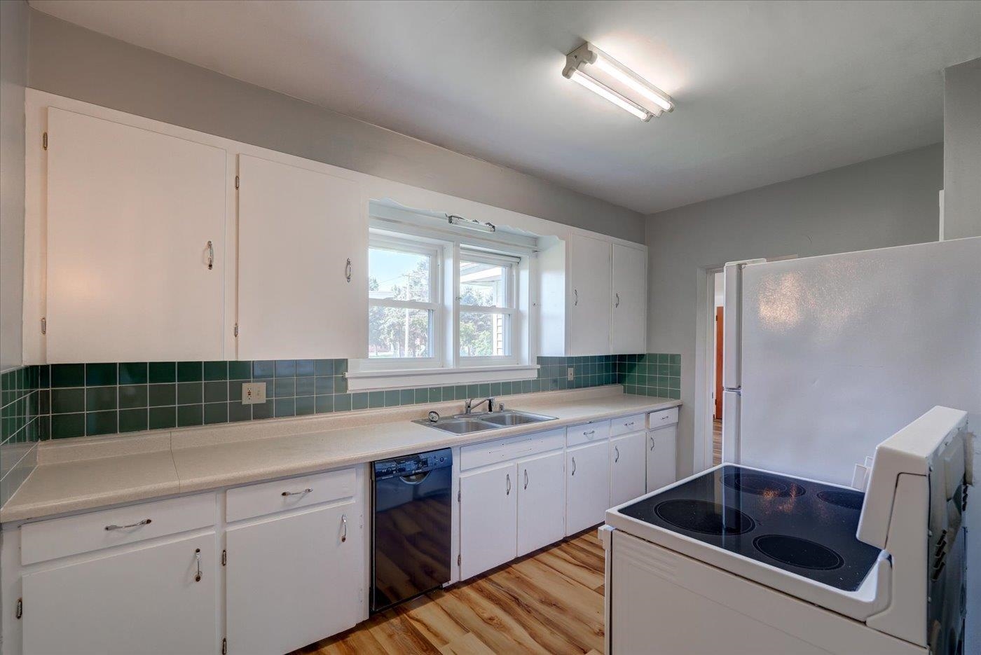 Kitchen with white cabinets, green tile backsplash, and an electric range beside a long counter.