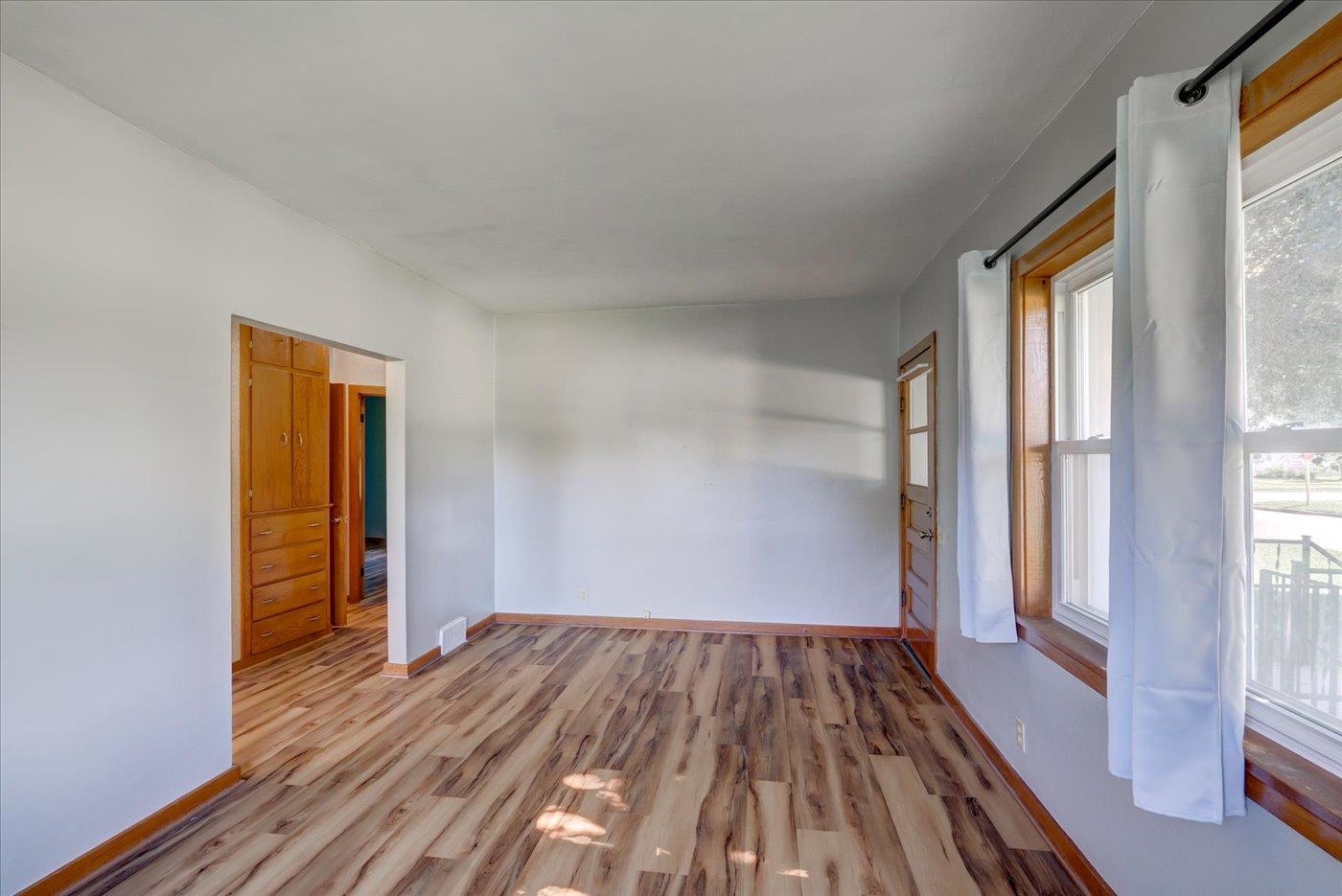Empty room with built-in wooden closets, wood-look flooring, and tall curtained windows.