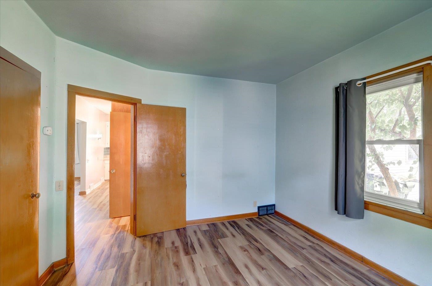 Empty room with wood-look flooring, pale blue walls, and a curtained window.