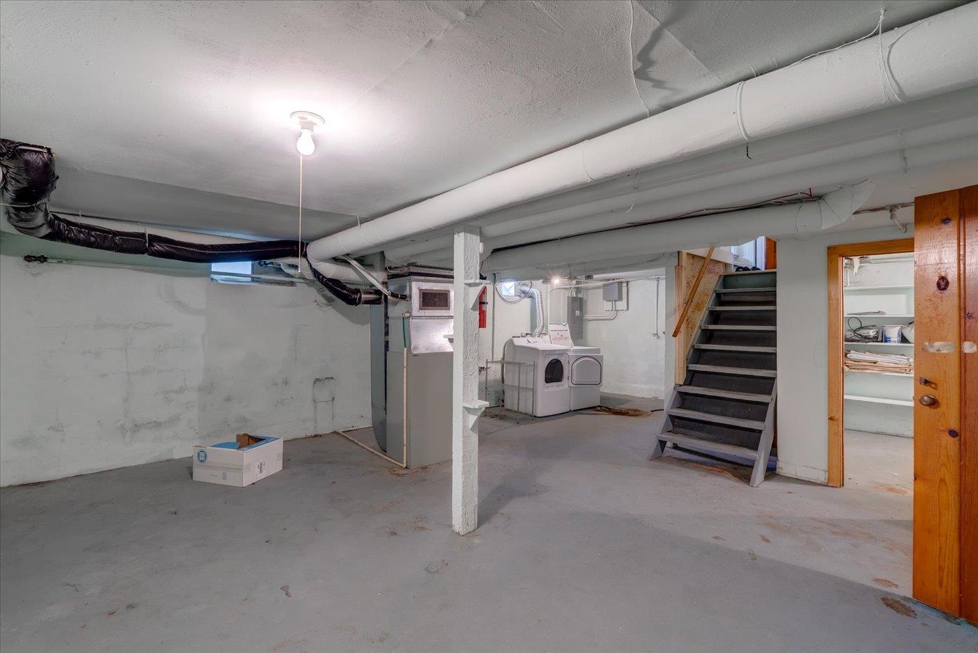 Unfinished basement with exposed ducts, a furnace, washer and dryer, and stairs.