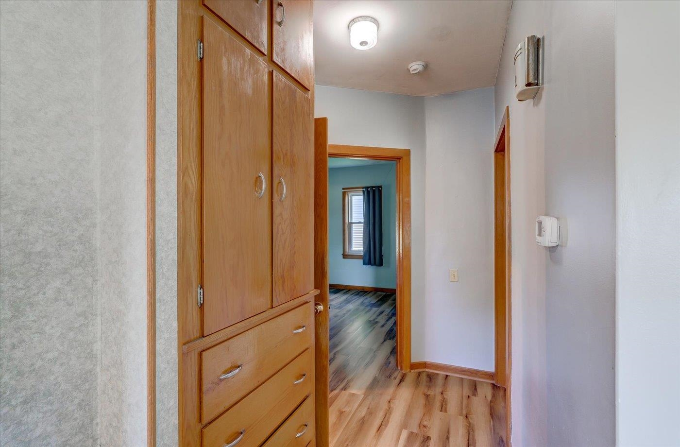 Hallway with built-in wooden cabinets and drawers, looking toward a room with a curtained window.