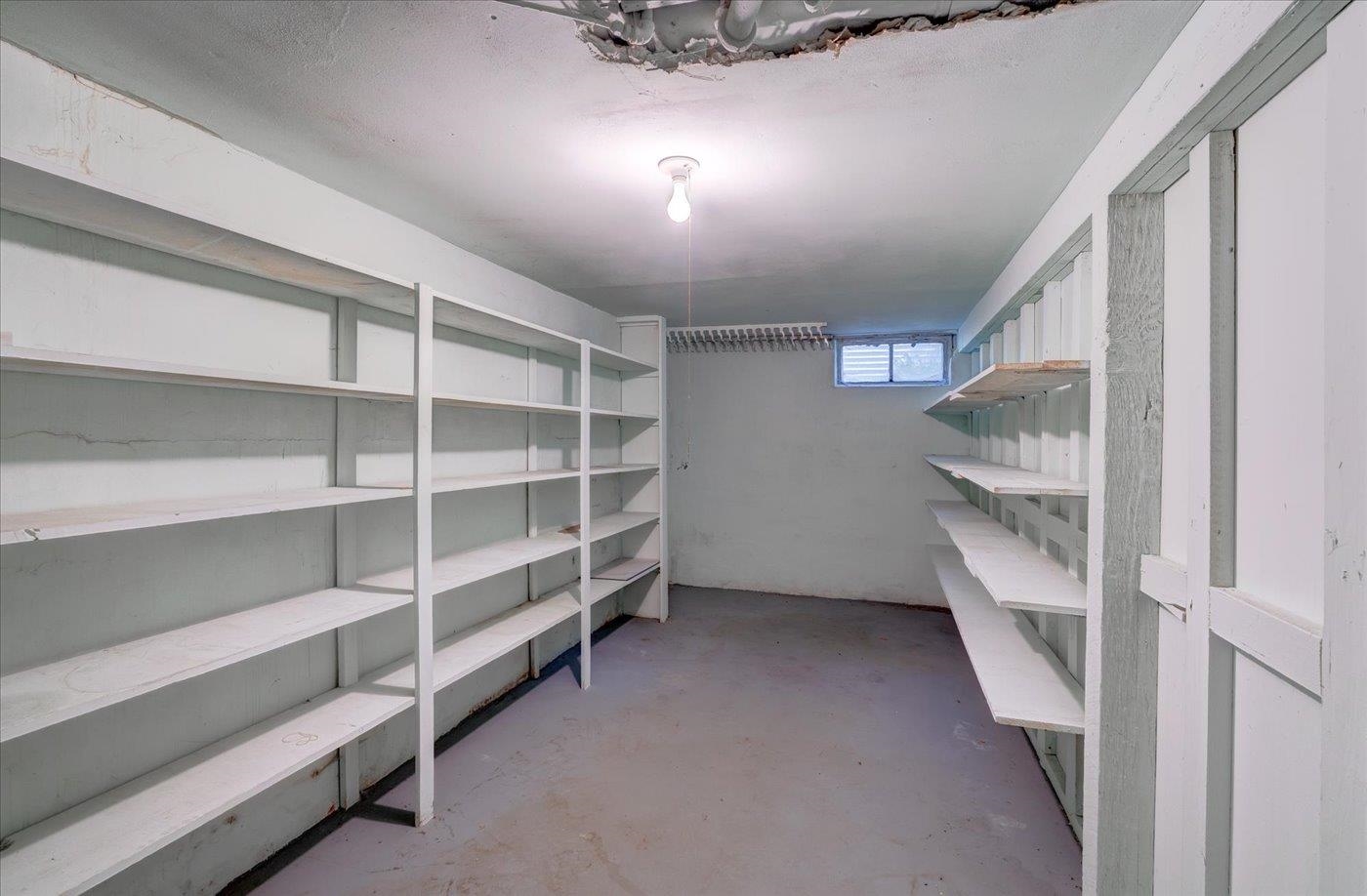 Empty storage room with built-in shelves along both walls and a small high window.
