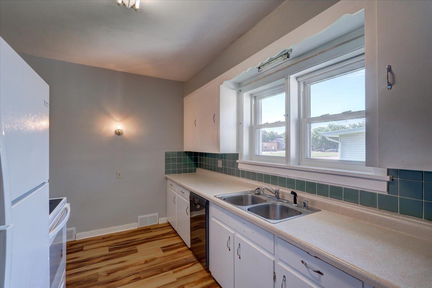 Kitchen with green tile backsplash, double sink, and two windows above the counter.