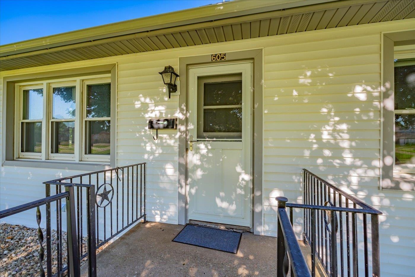 White-sided home entrance with number 605 above the door and black metal porch railings.