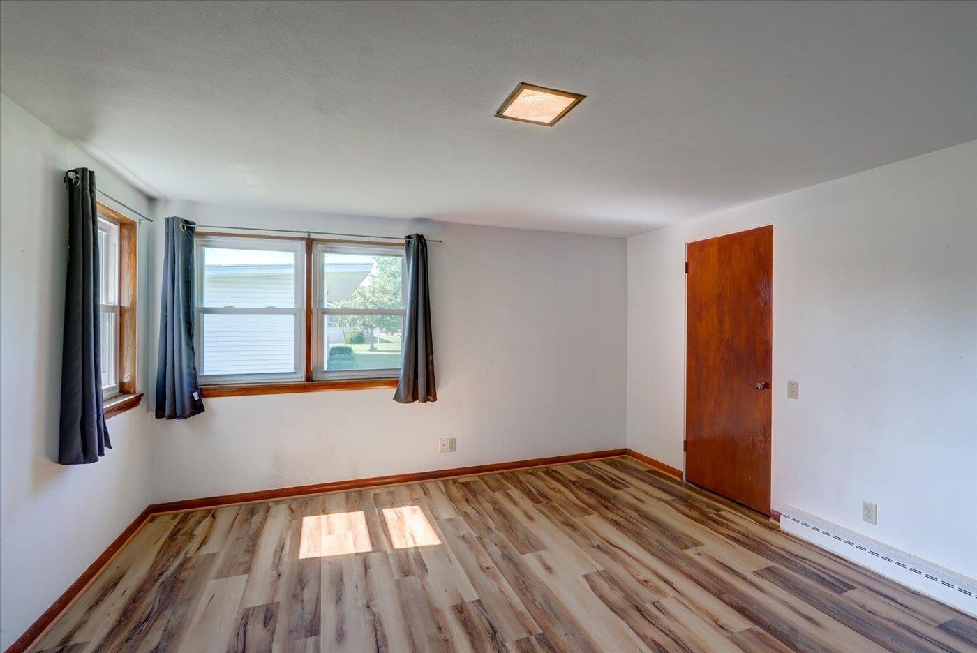 Empty room with wood-look flooring, dark trim, and two curtained windows.