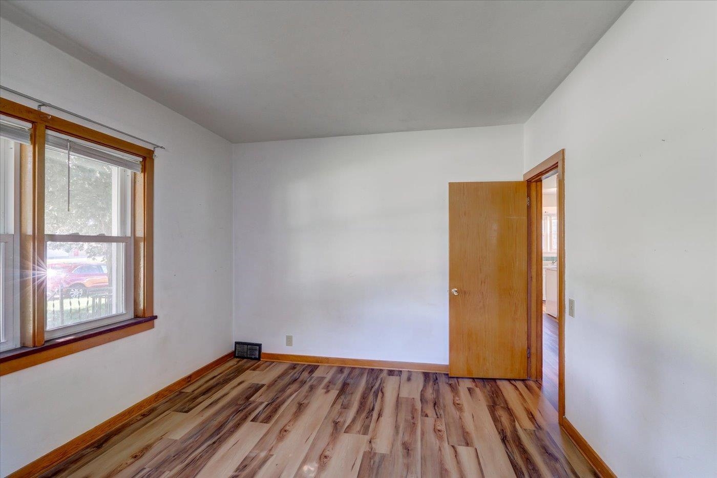 Empty room with multicolored plank flooring, wood-trimmed window, and open doorway.