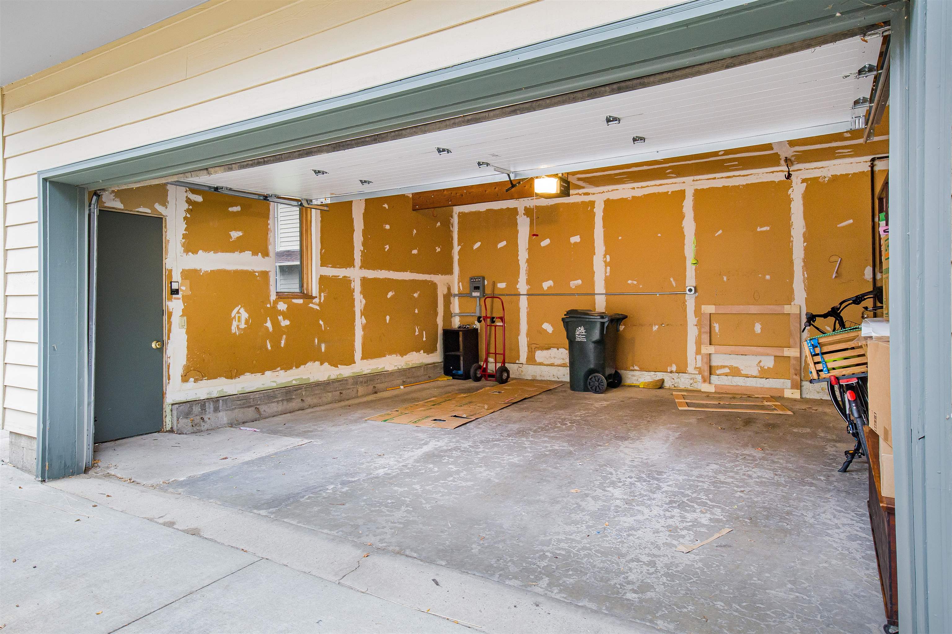 Unfinished garage with a raised overhead door, patched walls, and a broad concrete floor.
