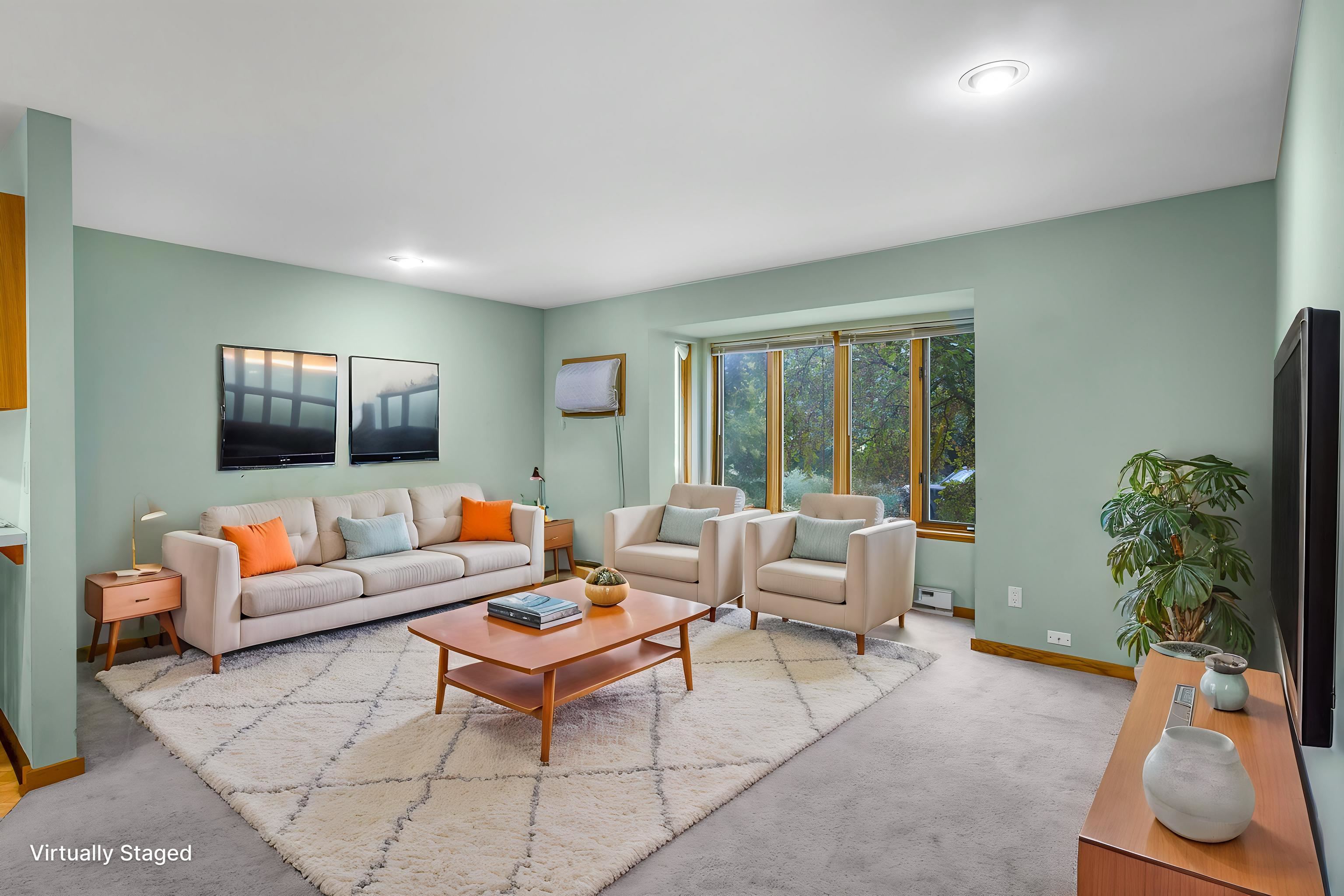 Virtually staged living room with cream seating, orange pillows, and a large window overlooking trees.