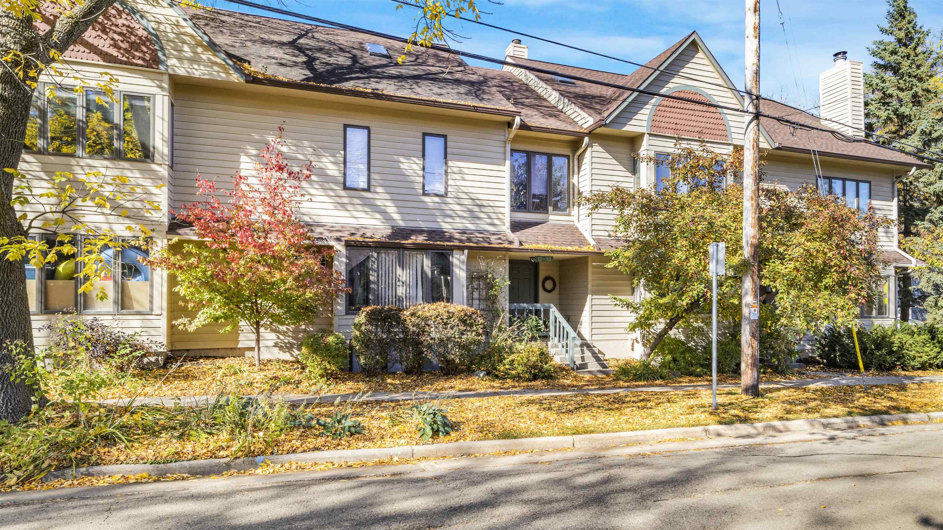 Multi-unit building with beige siding, a covered entrance, front steps, and autumn foliage.