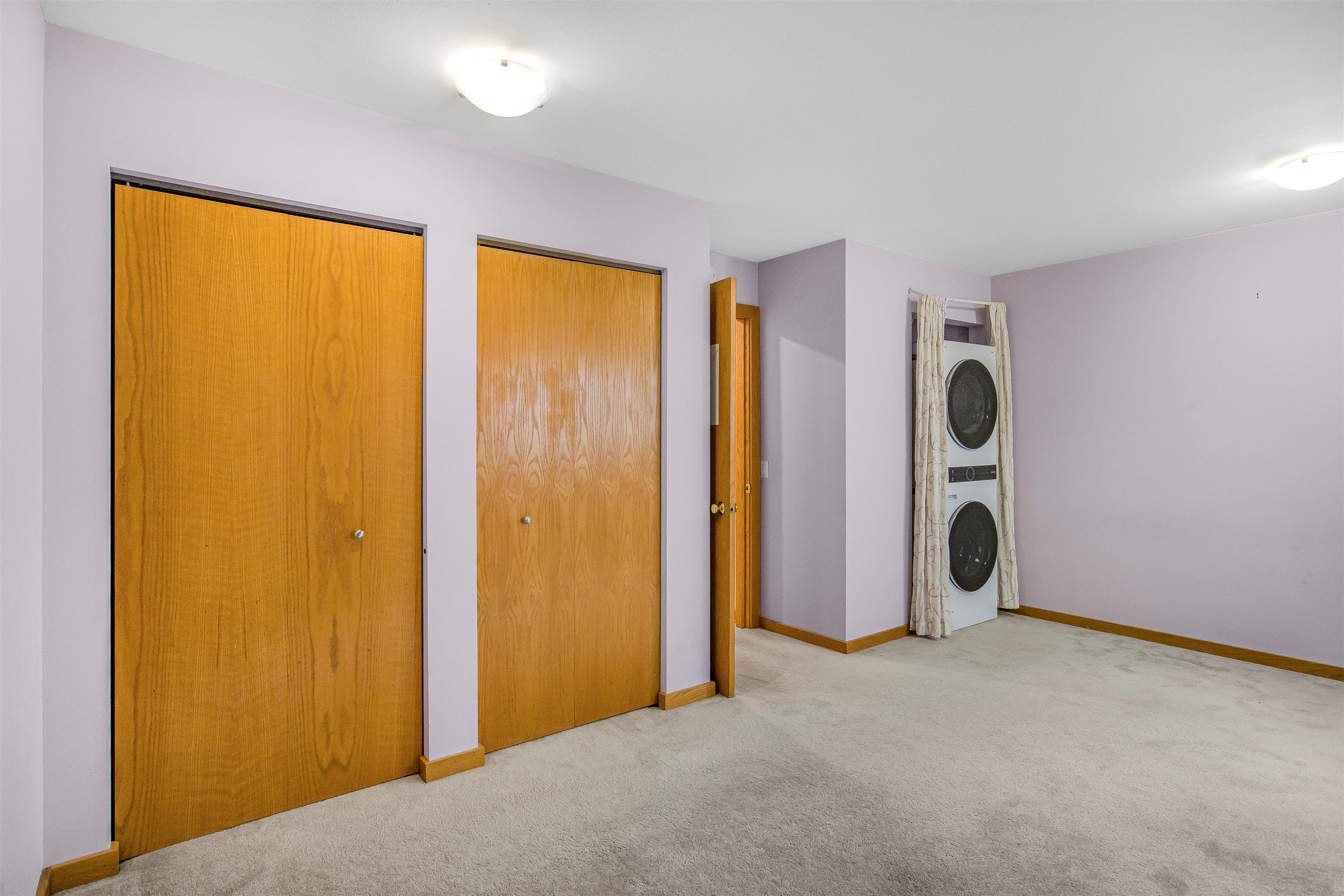 Carpeted room with wooden closet doors and a curtained stacked washer and dryer.