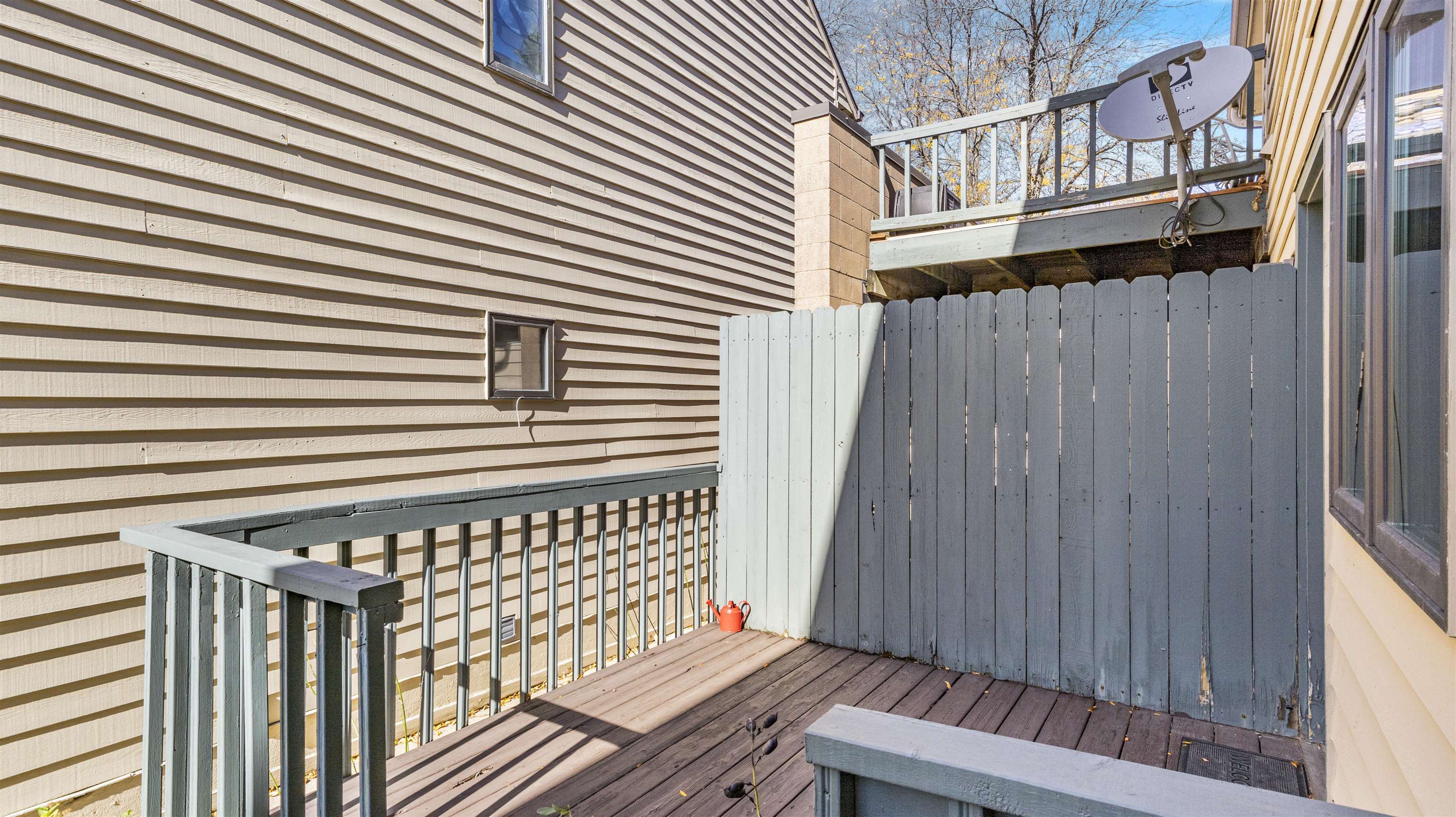 Wooden deck with gray privacy fencing and railings beside beige-sided homes.