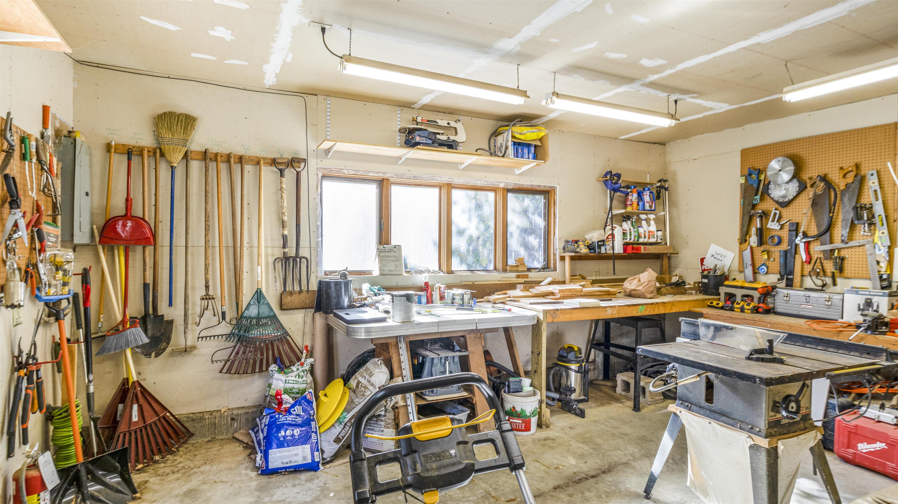 Workshop with wall-mounted tools, lumber-covered workbench, table saws, and a lawn mower.