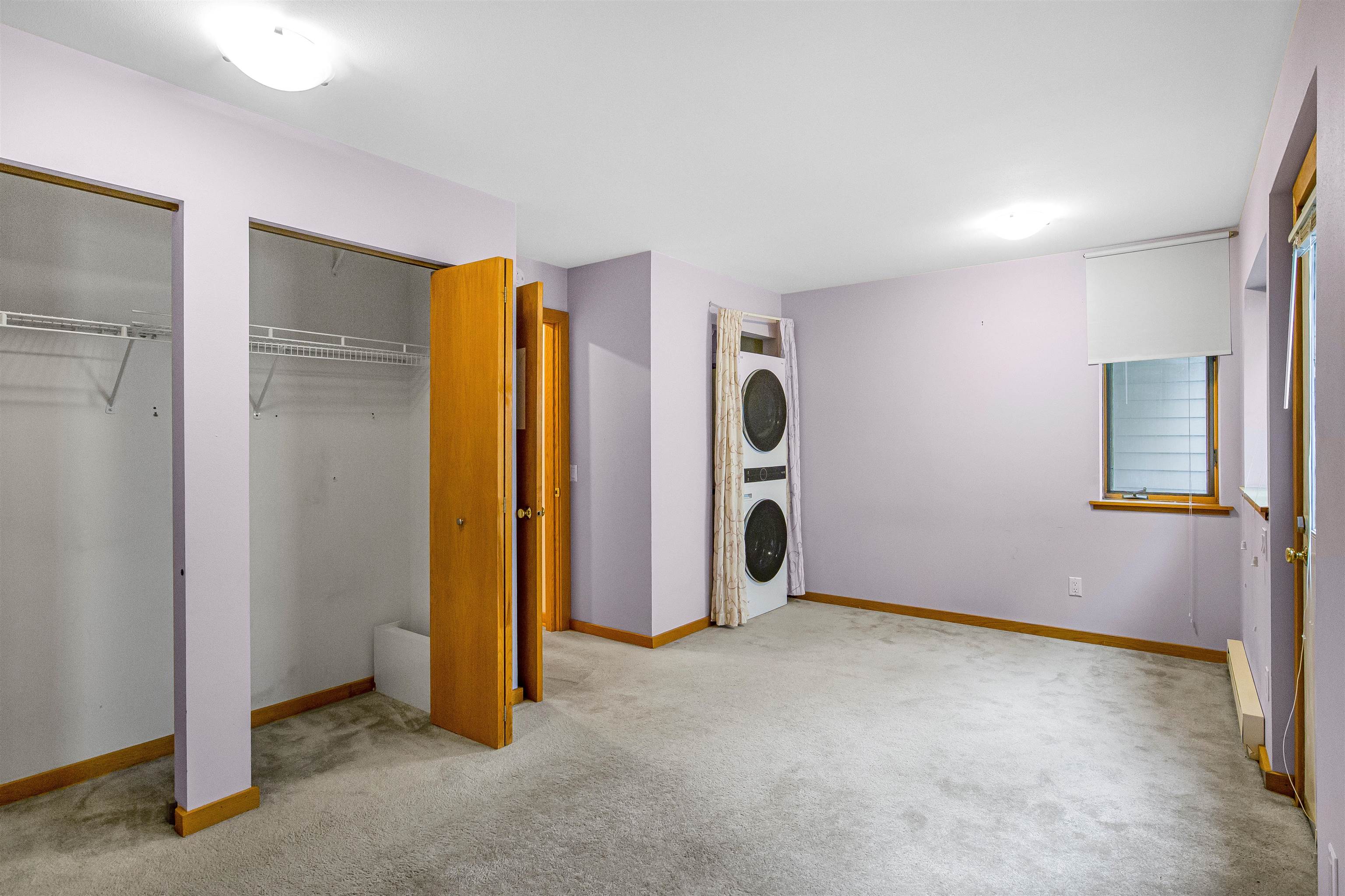 Empty carpeted bedroom with open closets and a stacked washer and dryer.