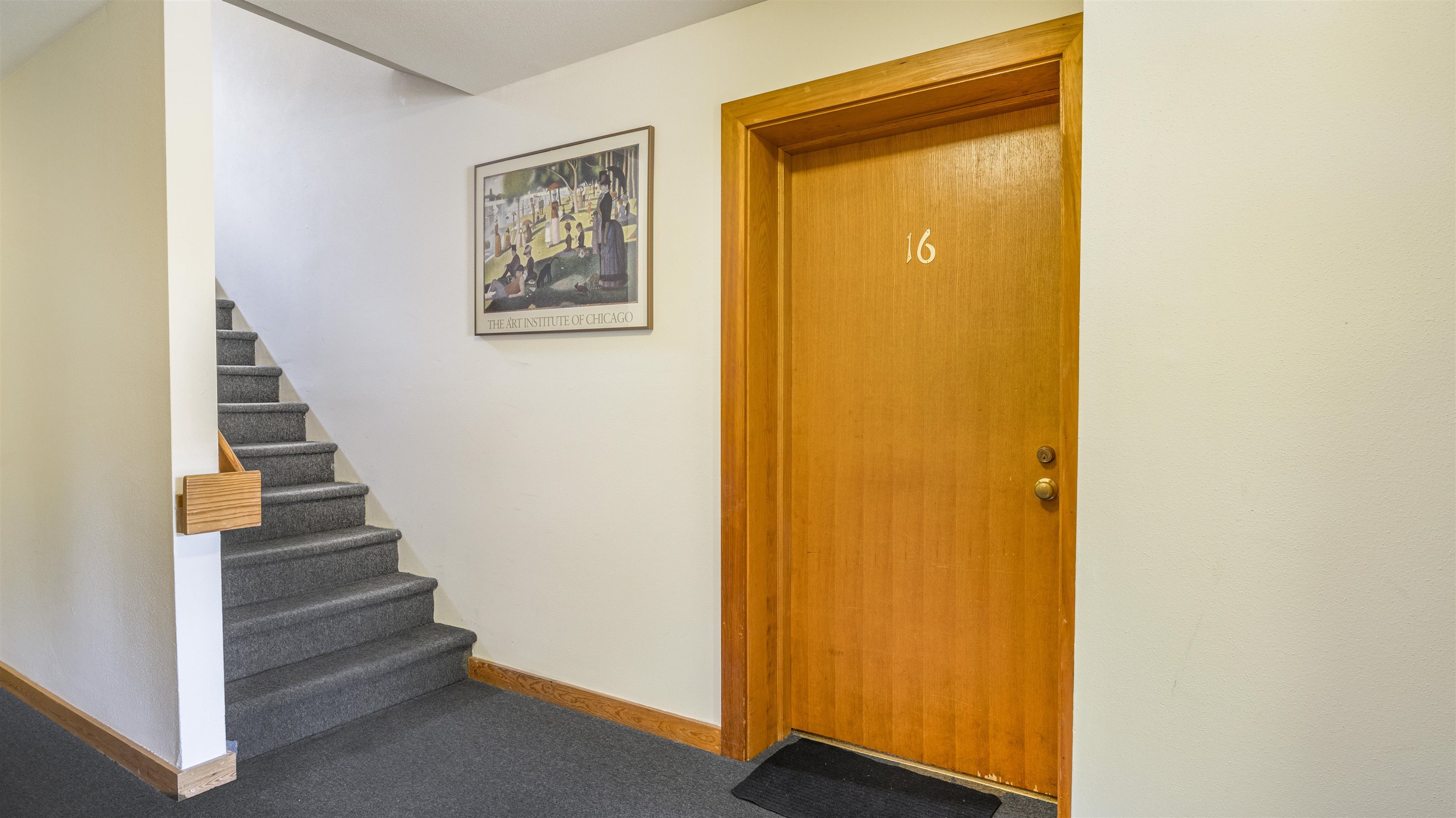 Entryway with a wooden door marked 16 beside gray carpeted stairs.