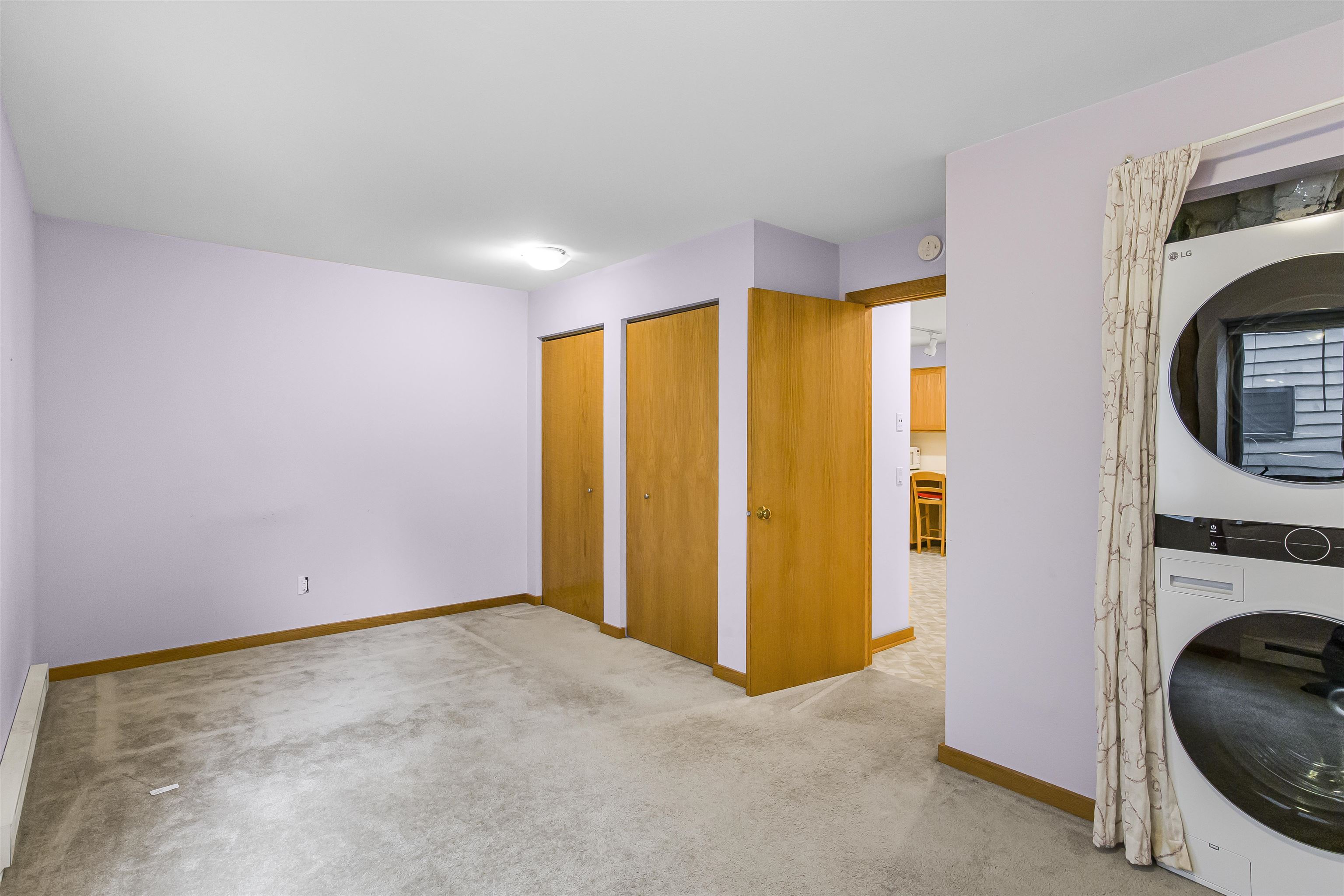 Empty carpeted room with wooden doors and a stacked washer and dryer behind a curtain.