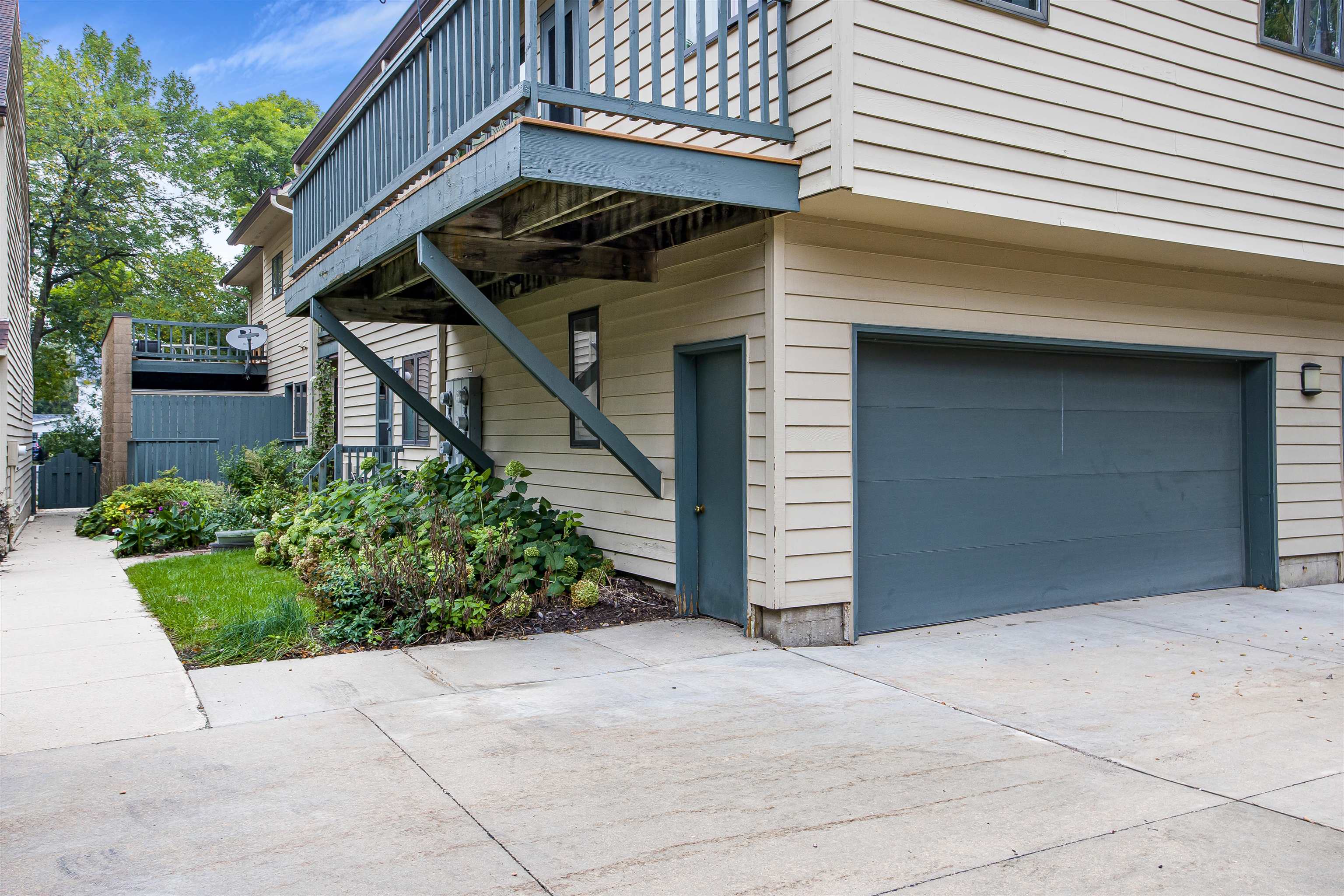 Home exterior with a raised deck, blue-gray garage door, and landscaped garden beds.